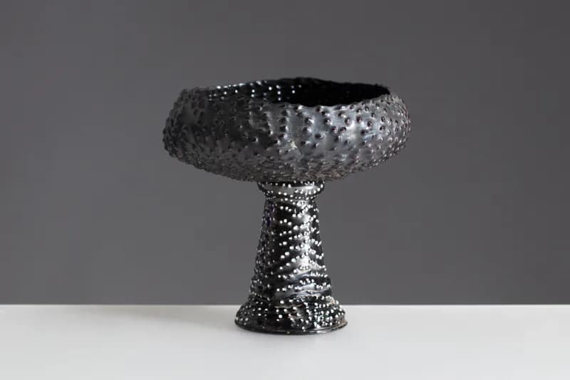 Sculptural metal pedestal table with textured spherical top and tapered stem base in dark metallic finish by R & Company.