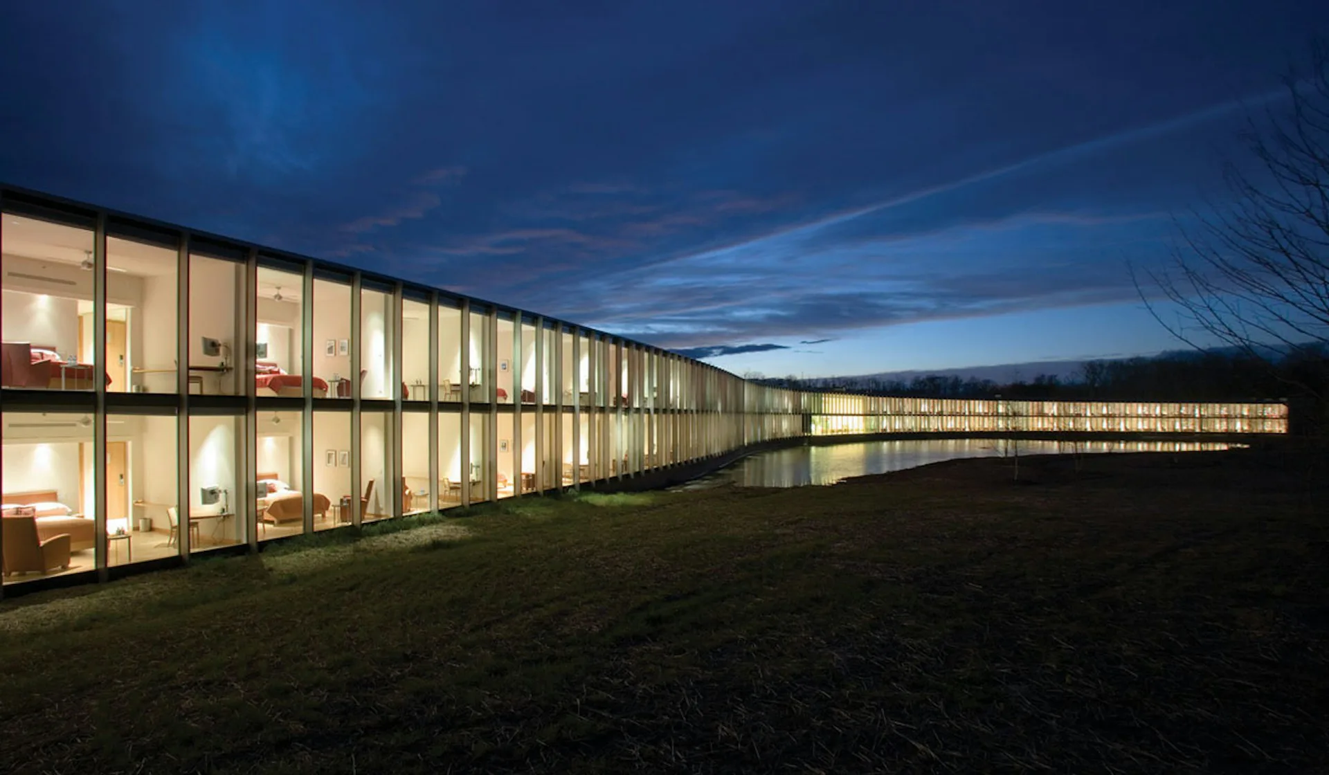 Modern institutional building with continuous glazed facade illuminated at dusk, linear form set against twilight sky by Rafael Vinoly Architects.