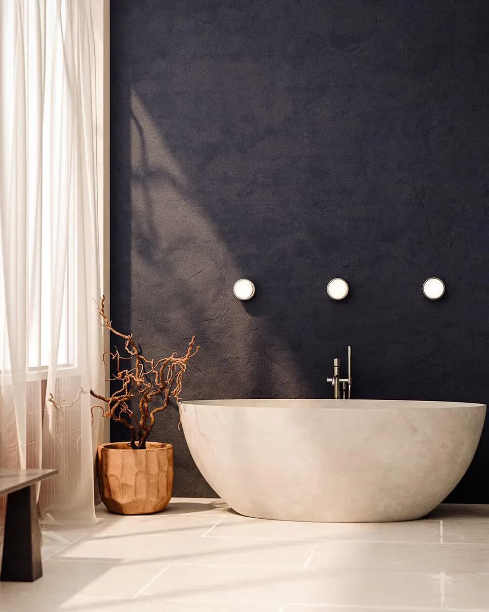 Minimalist bathroom interior featuring a sculptural white stone bathtub, dark charcoal wall, three circular wall lights, wooden decorative vessel, and cream curtains by RBW.