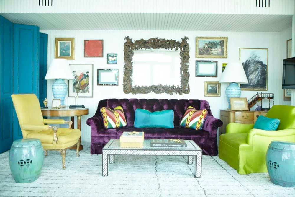 Vibrant living room featuring a purple velvet sofa, lime green armchair, turquoise accents, and gallery wall with botanical prints by Redd Kaihoi.