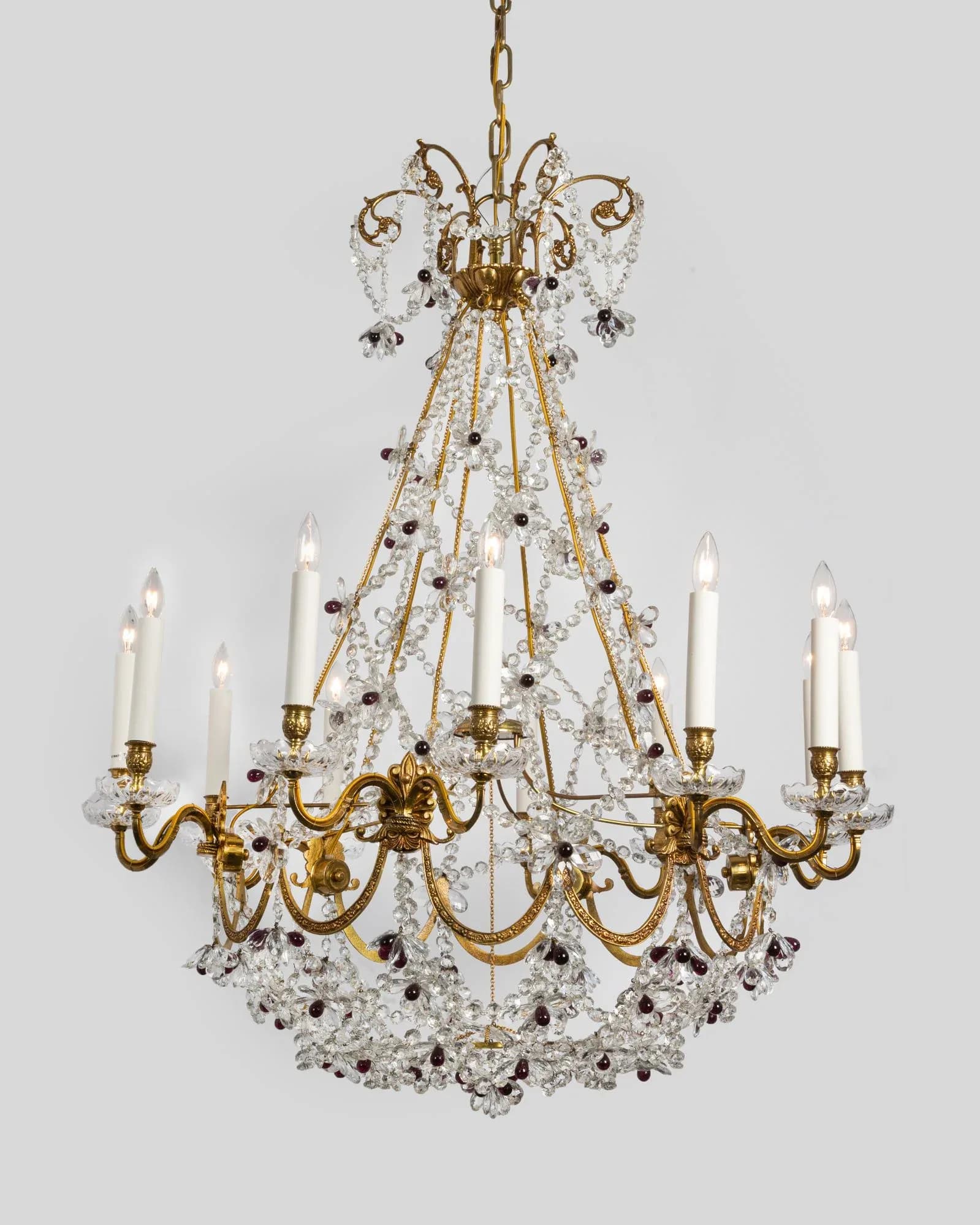 Ornate brass chandelier with crystal drops and eight candle arms suspended against a neutral background, by Remains Lighting Company.