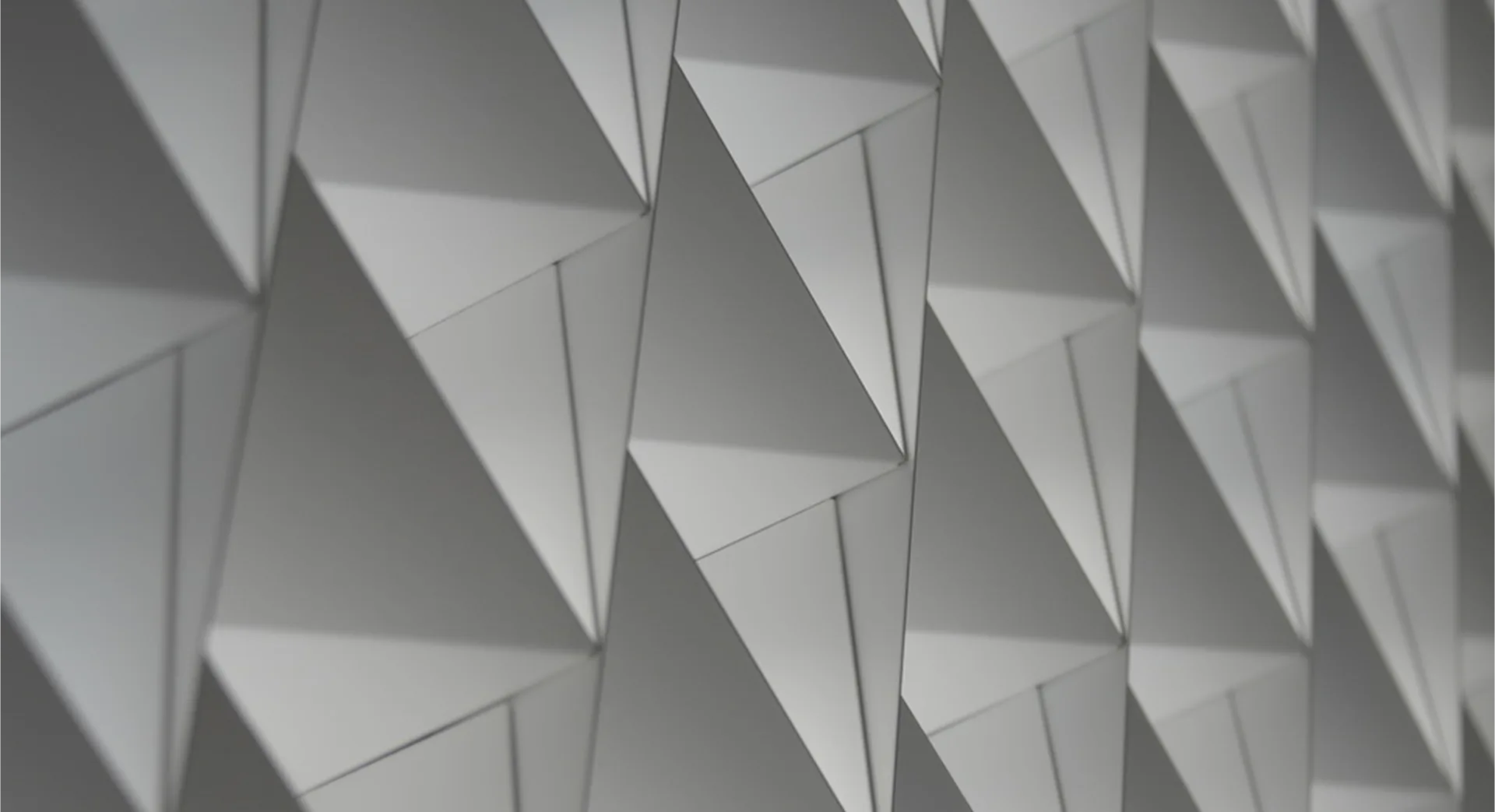 Geometric wall installation featuring repeating triangular panels with dynamic shadow play creating dimensional depth, by Renfro Design Group.