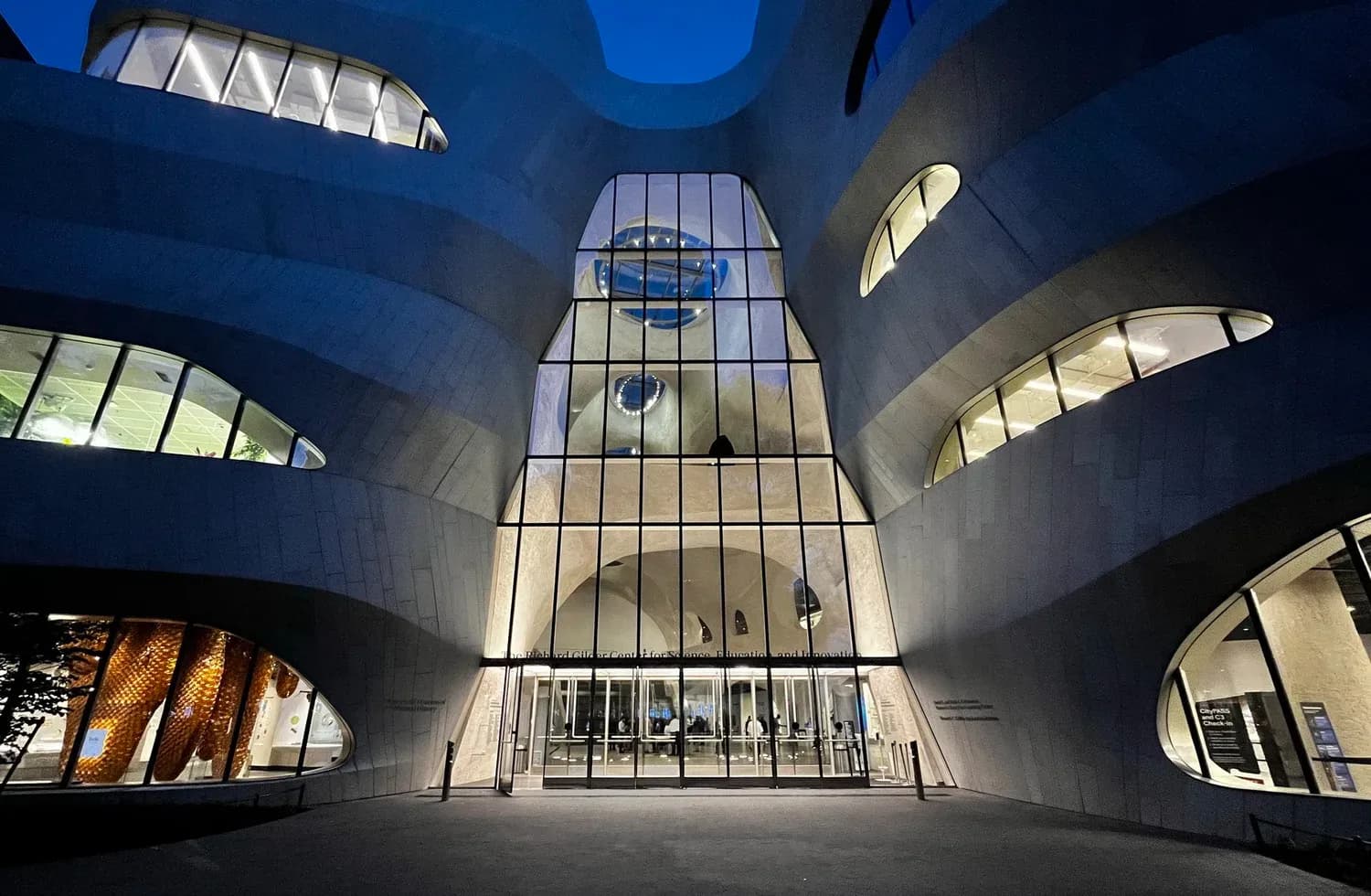 Illuminated atrium with curved concrete walls, gridded glass windows, and symmetrical oval openings creating a dramatic interior space by Renfro Design Group.