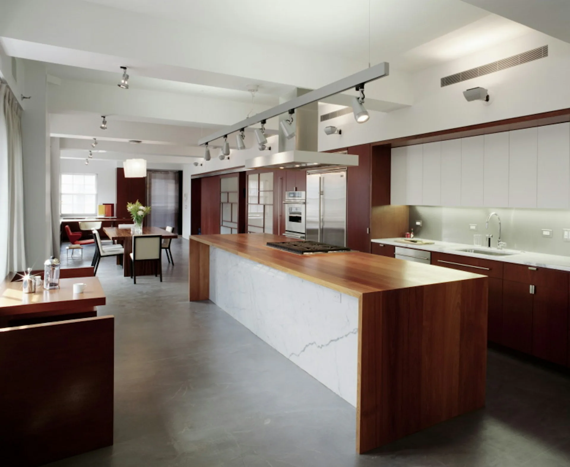 Modern open-plan kitchen and dining area with dark wood cabinetry, white marble island countertop, and polished concrete flooring by Resolution: 4 Architecture.