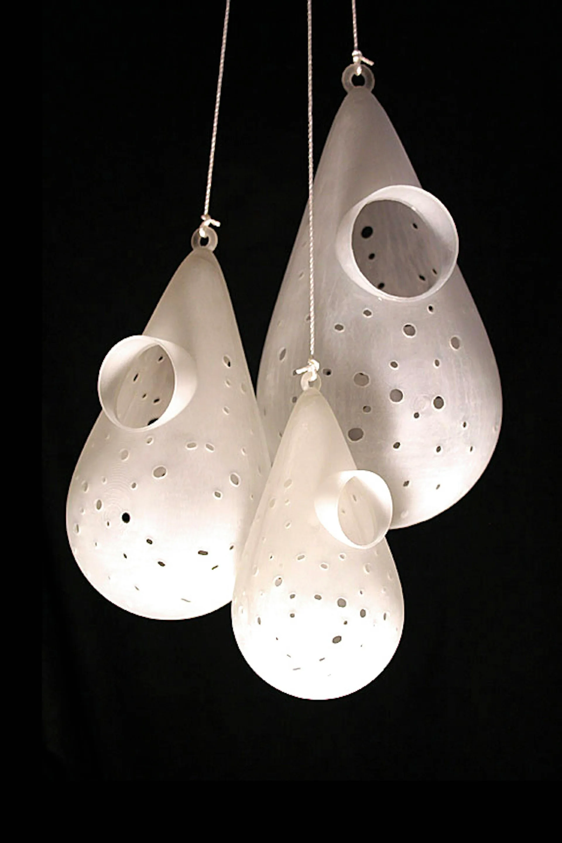 Three suspended ceramic pendant lights with perforated surfaces and circular openings, illuminated against a black background, designed by Resolution: 4 Architecture.