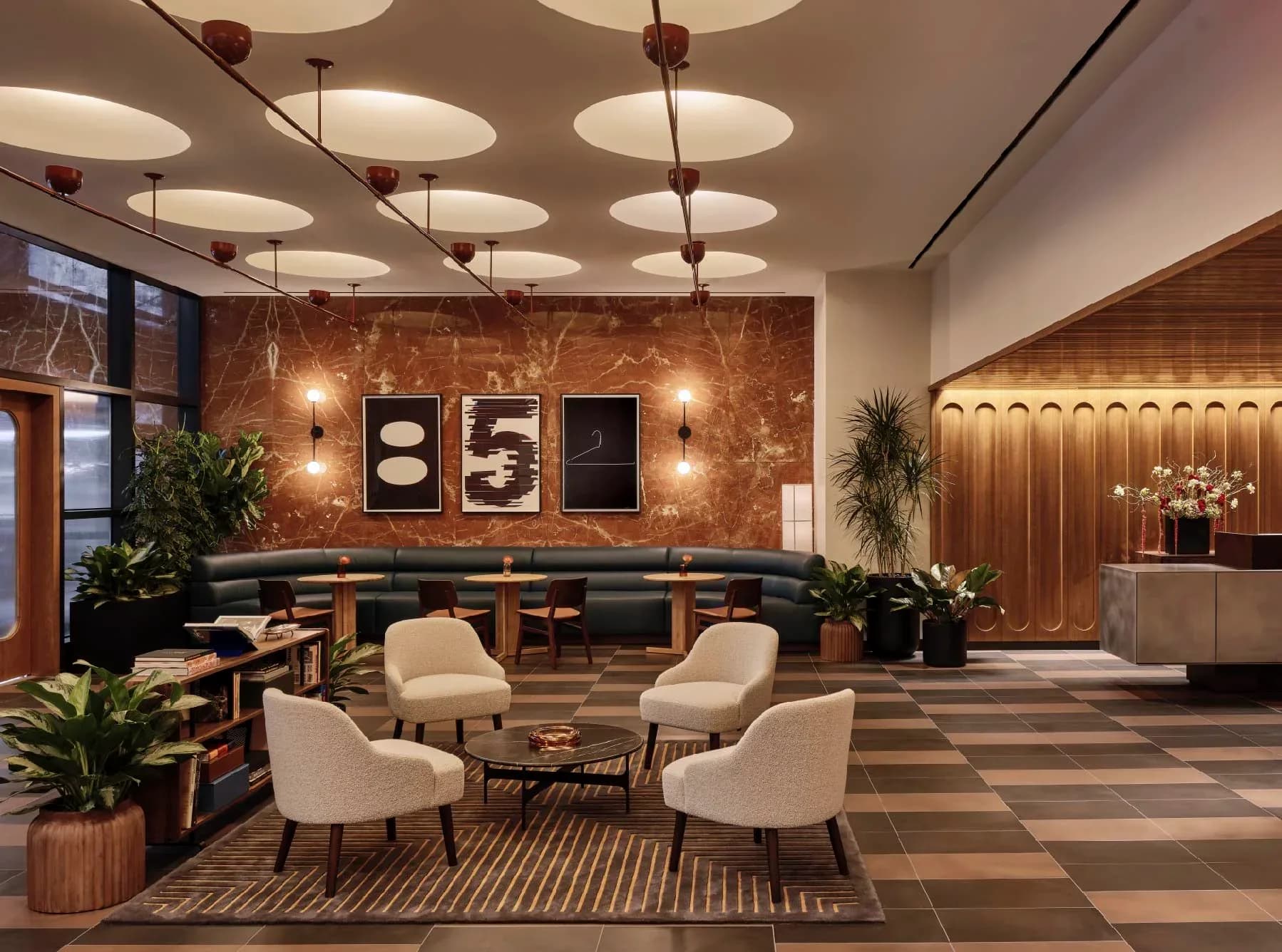 Modern luxury lobby with warm wood accent wall, geometric ceiling panels with integrated lighting, cream seating arrangement, and decorative abstract artwork by Reveal Design Group.