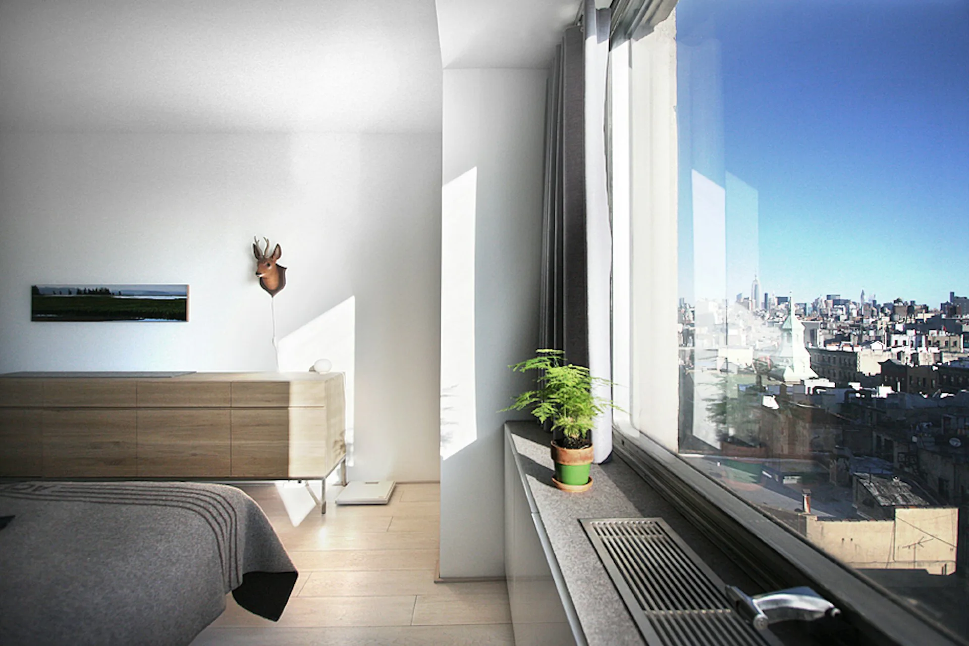 Modern bedroom with wooden bed, floor-to-ceiling windows overlooking city skyline, minimalist décor, and natural light by Rice+Lipka Architects.
