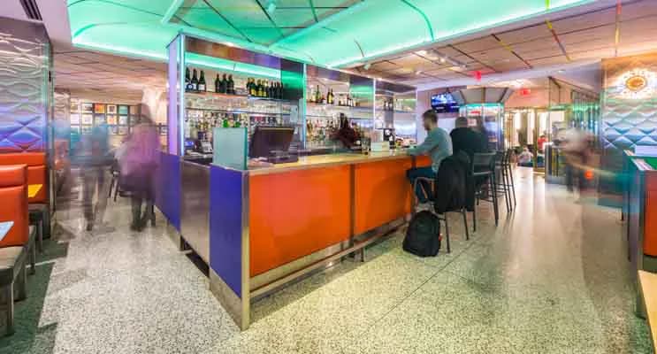 Colorful modern bar interior with vibrant orange, blue, and green elements, polished concrete floors, and ambient lighting by Richard Bloch Architect.