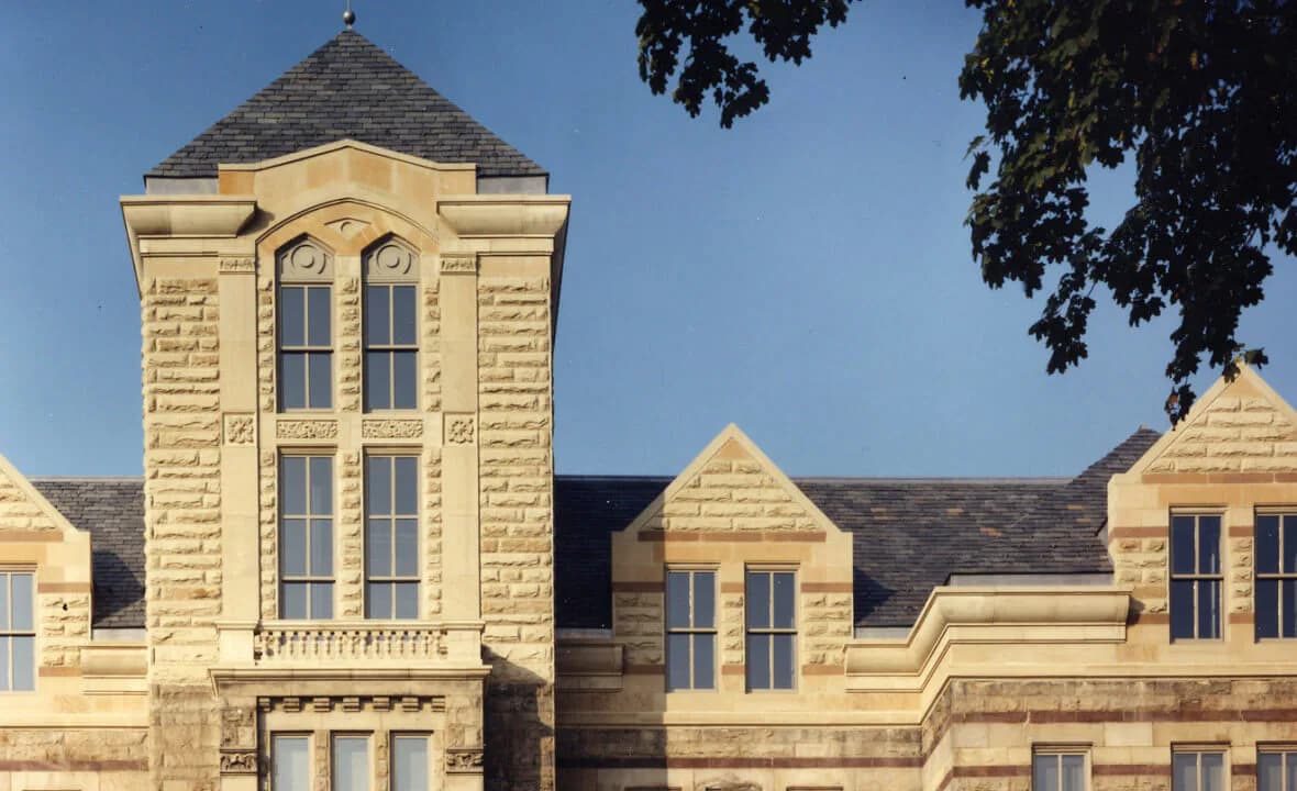 Cream-colored stone institutional building facade featuring a prominent central tower with paired windows and slate roof, designed by Richard McElhiney Architects LLC.