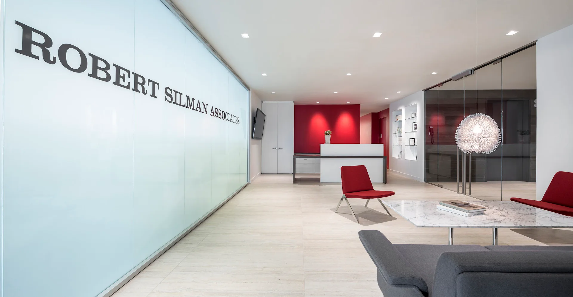 Modern office reception area with red accent wall, minimalist furniture, and clean geometric forms designed by Rise Projects.