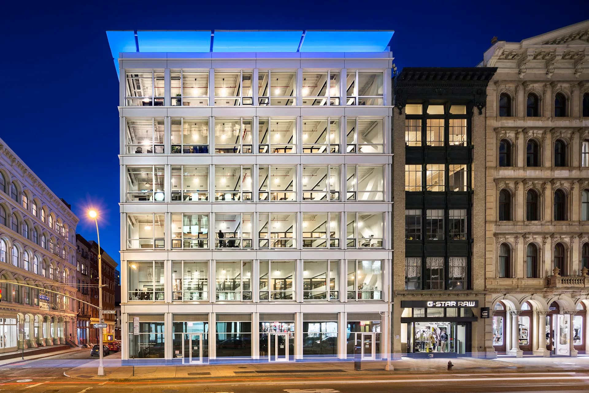Illuminated modern commercial building with glass facade and white frame on historic New York street, designed by RKTB Architects, P.C.
