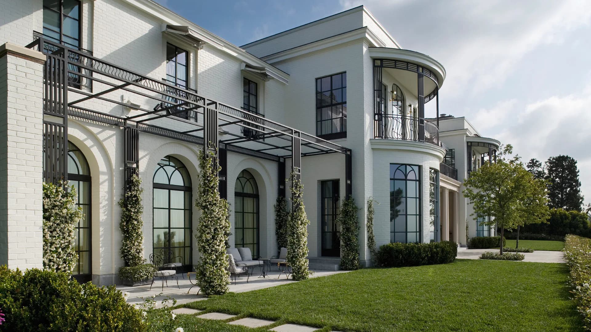 Modern neoclassical residence with white facade, arched windows, ivy-covered walls, and manicured lawn by Robert A.M. Stern Architects.
