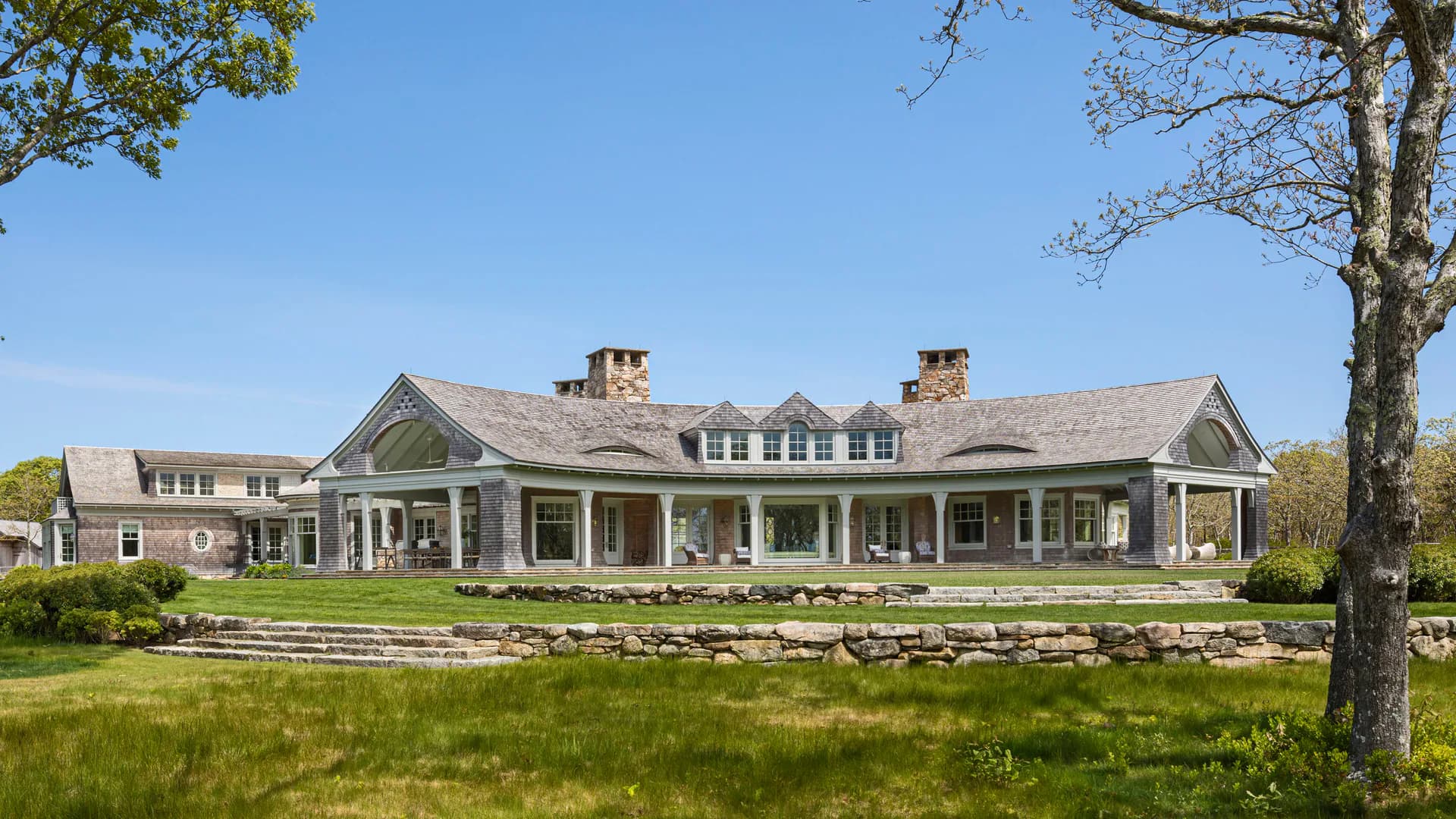 Expansive residential estate with symmetrical shingled façade, columned porches, multiple gables, and manicured lawn by Robert A.M. Stern Architects.