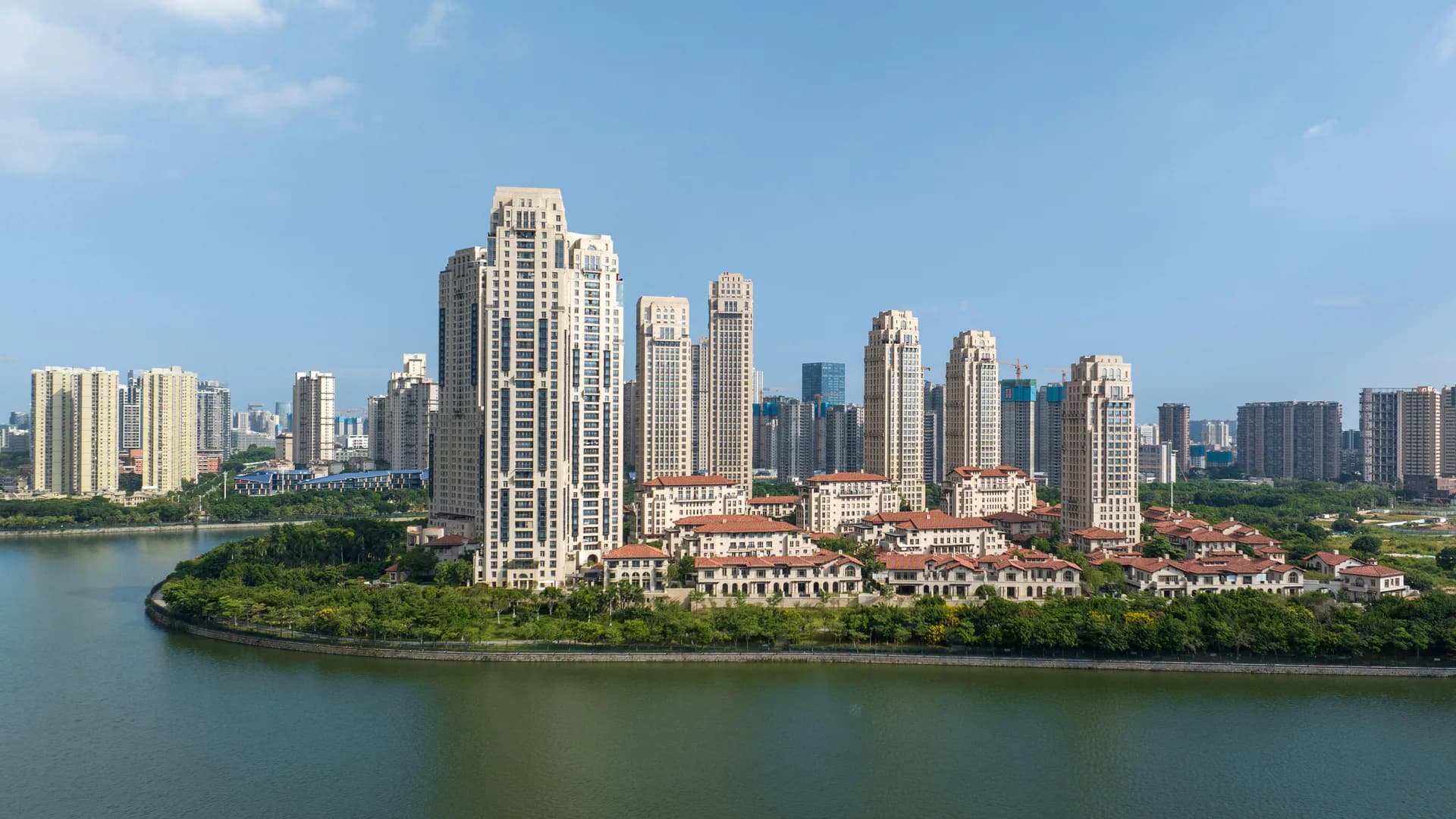 Waterfront residential and mixed-use development featuring cream-colored towers with classical architecture rising above tree-lined green space along a river bend, designed by Robert A.M. Stern Architects.