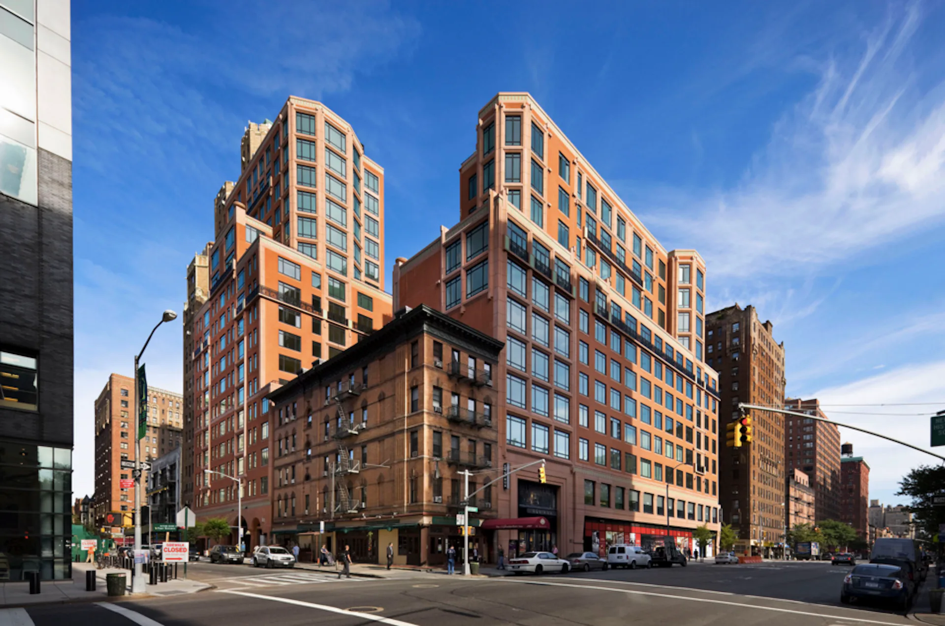Urban mixed-use development featuring orange and brick residential towers with street-level retail, photographed under blue sky by Robert A.M. Stern Architects (RAMSA).
