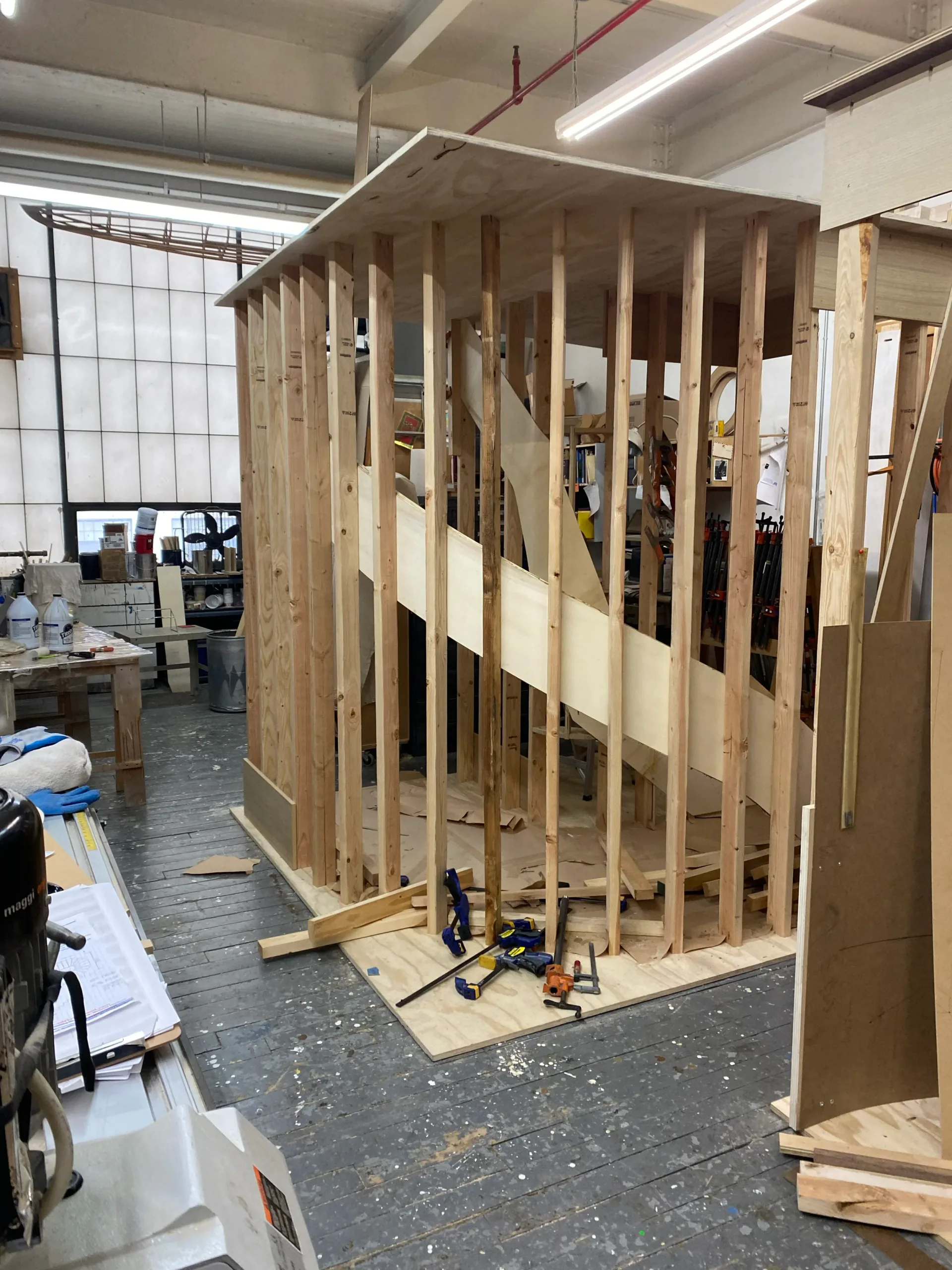 A wood-frame architectural installation under construction in a workshop, featuring exposed timber studs and beams with plywood panels, showcasing custom carpentry work by Robert Kalka Custom Woodworking.
