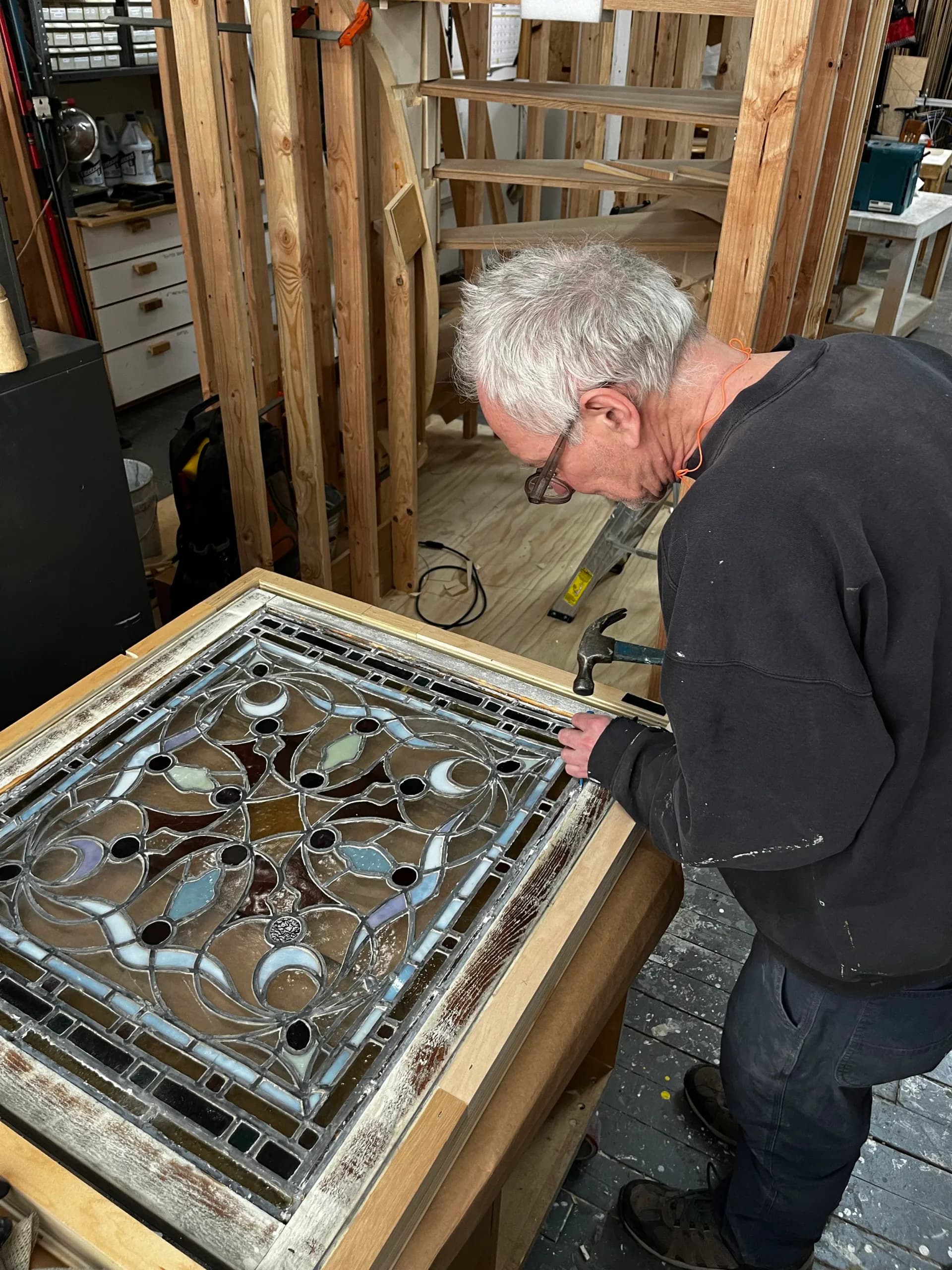 Craftsman examines ornate leaded glass window panel with blue and amber tones set in wooden frame by Robert Kalka Custom Woodworking.