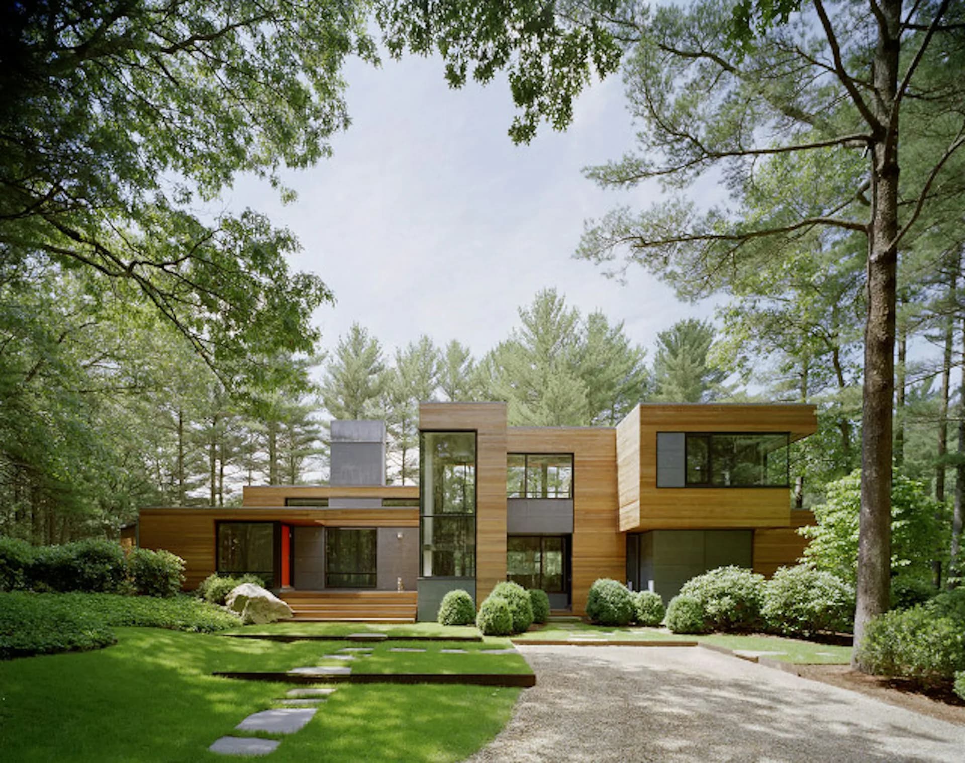 Modern residential home with warm wood and metal cladding nestled among mature trees, featuring clean geometric lines and large windows, by Robert Young Architects.