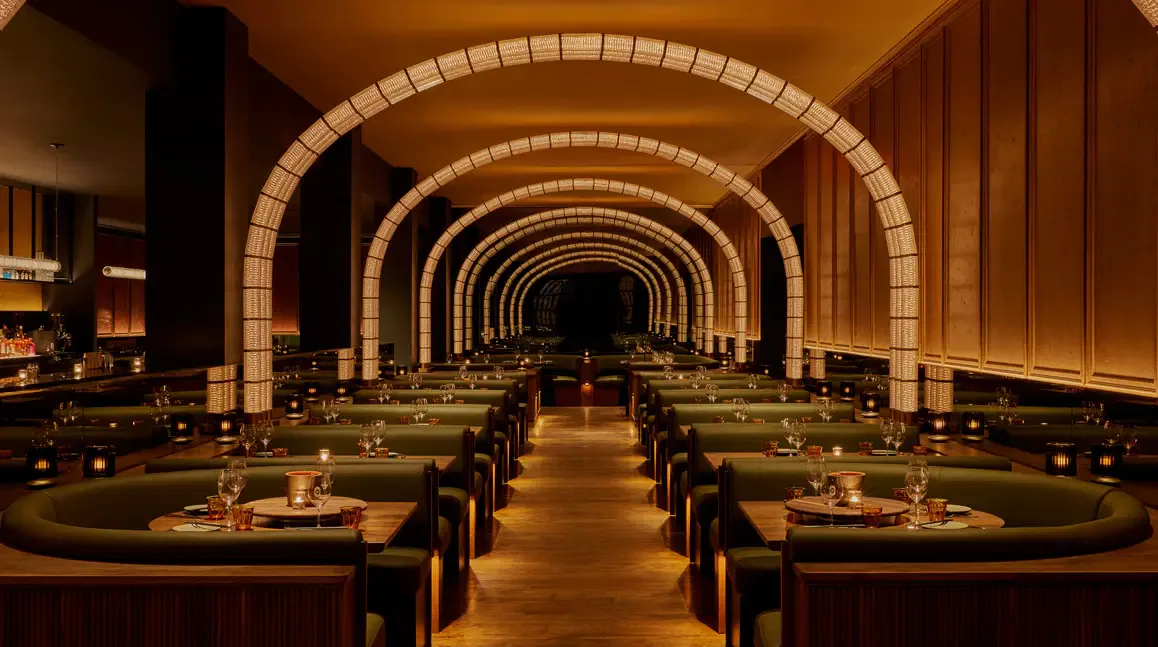 Elegant dining restaurant with repeating arched brick ceilings, ambient lighting, and table settings along a symmetrical corridor by Rockwell Group.