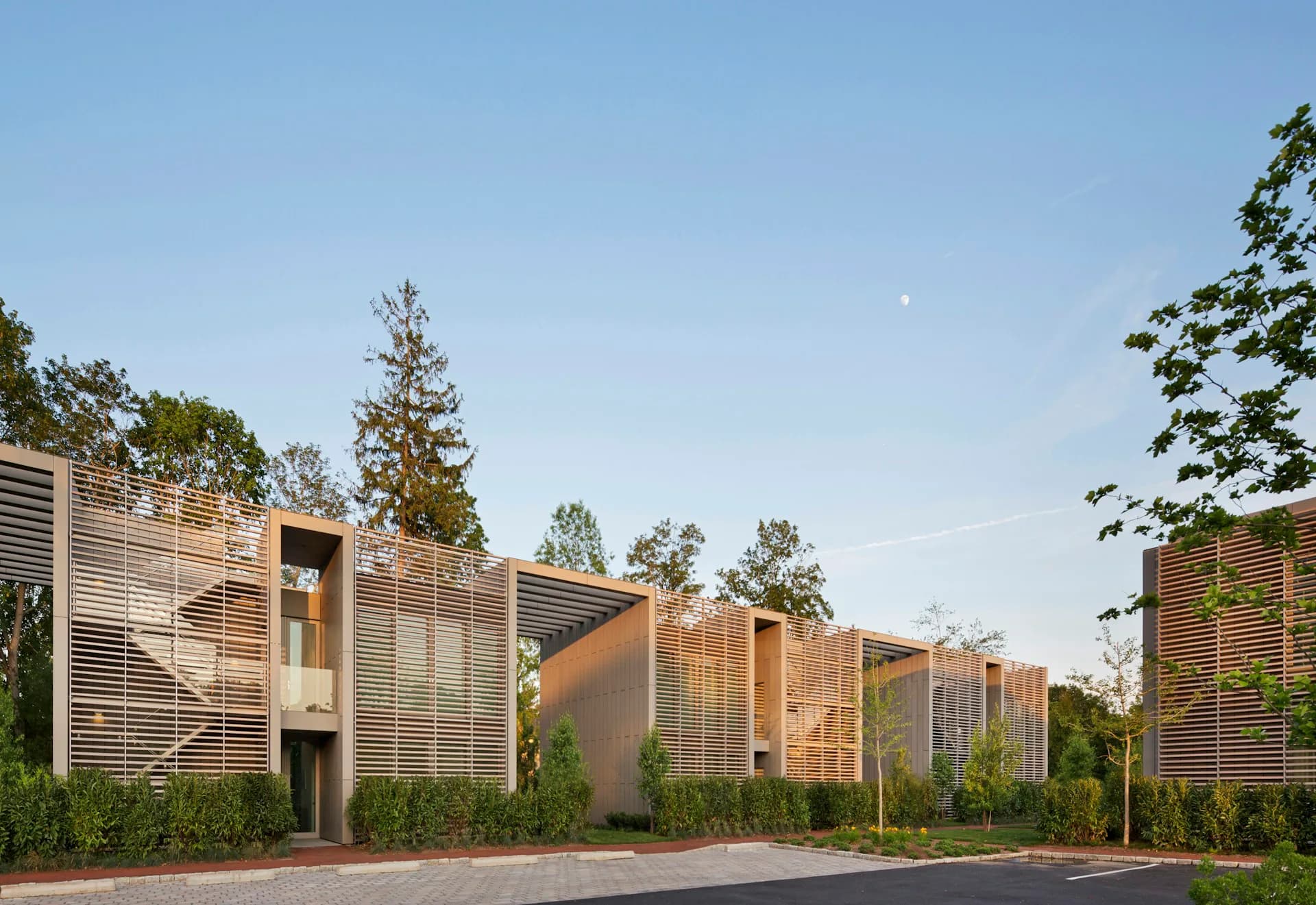 Residential complex with wooden slatted facades and warm earth tones arranged in staggered volumes along a brick courtyard, designed by Roger Ferris + Partners.