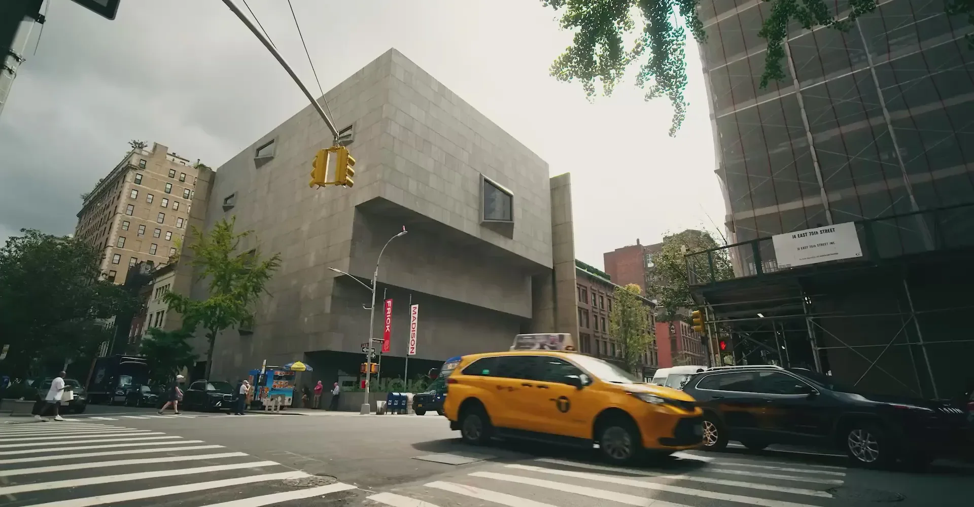 Street-level urban architecture featuring a geometric concrete building with horizontal planes, yellow taxi and dark vehicle at crosswalk, surrounded by mixed-height buildings by Roman and Williams.