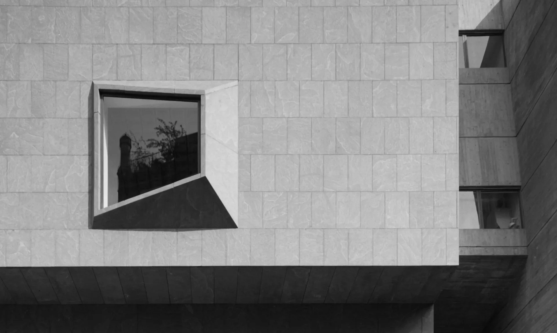 Minimalist architectural facade in monochromatic tones featuring a geometric window with dramatic shadow, showcasing clean lines and modernist design by Roman and Williams.