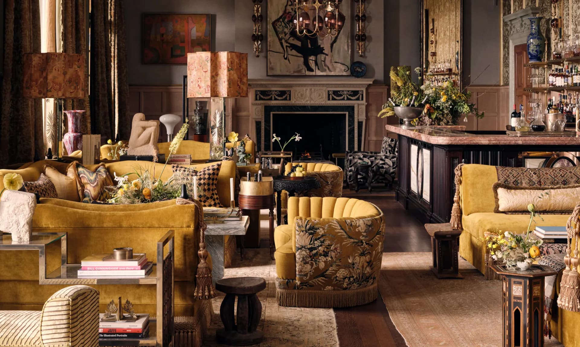 Luxurious living room with golden-yellow upholstered furniture, dark wood accents, fireplace, and warm lighting designed by Roman and Williams.
