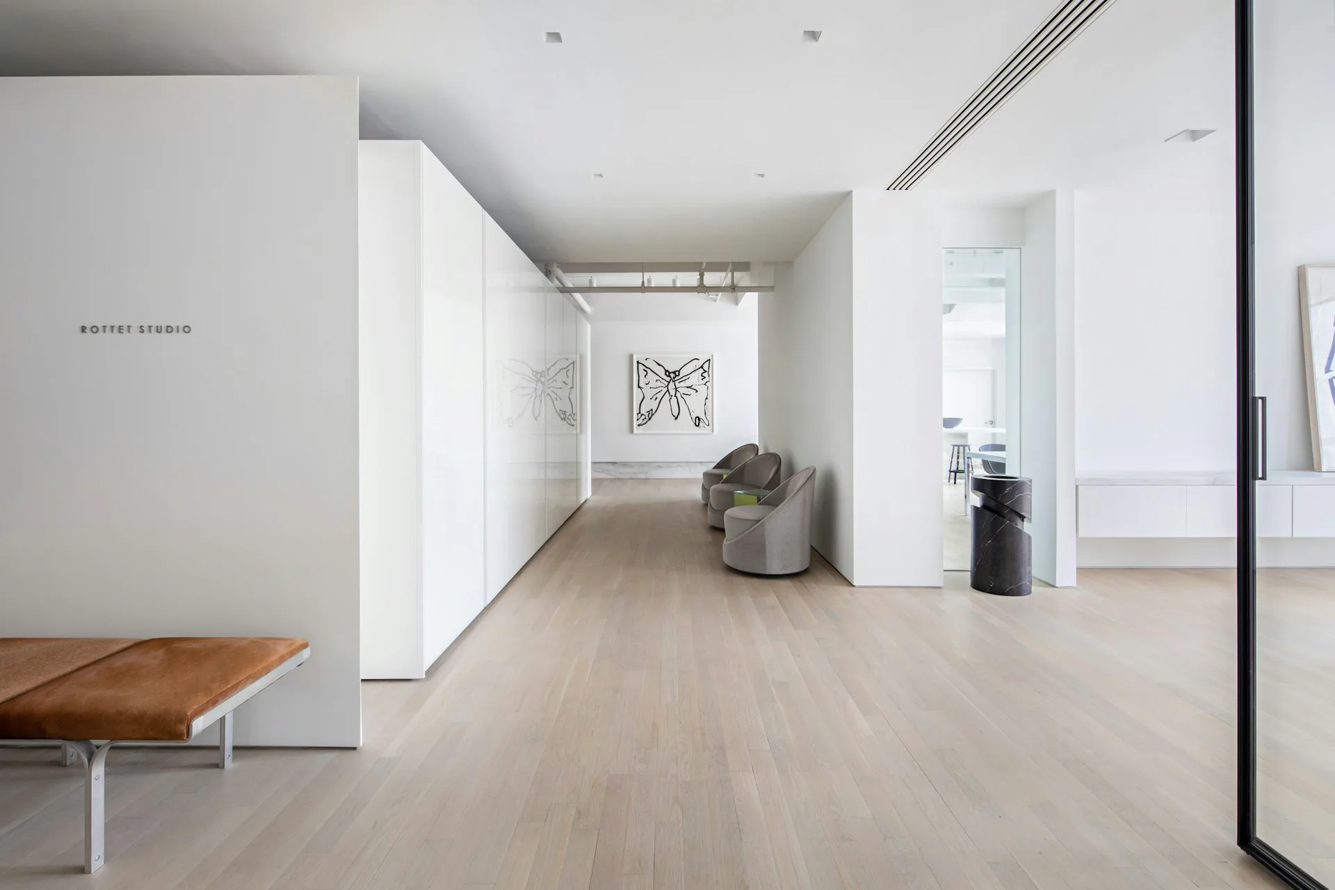 Minimalist commercial interior with light wood flooring, white walls, and clean lines, featuring a sculptural white partition and modern furnishings by Rottet Studio.