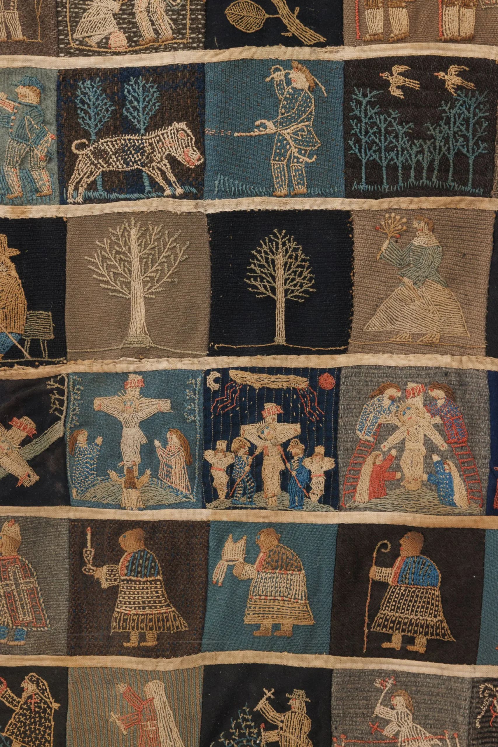 Textile rug detail showcasing traditional woven patterns with figures, animals, trees, and geometric designs in muted earth tones and blues by Rug & Kilim.