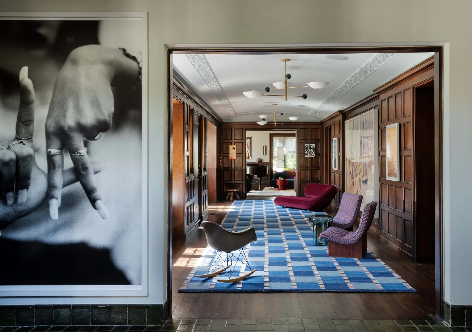 Residential hallway corridor with rich wood paneling, geometric blue and white patterned rug by Rug & Kilim, purple mid-century modern chairs, and natural sunlight throughout the refined interior.