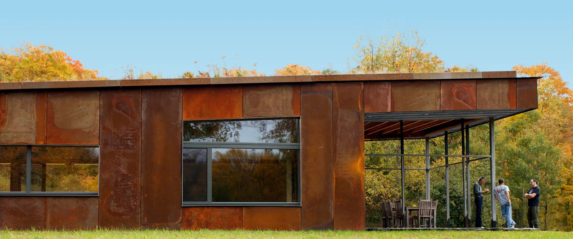 Modernist residential structure clad in weathered steel with expansive glazing overlooking autumn landscape, featuring clean geometric forms by Ryall Sheridan Architects.