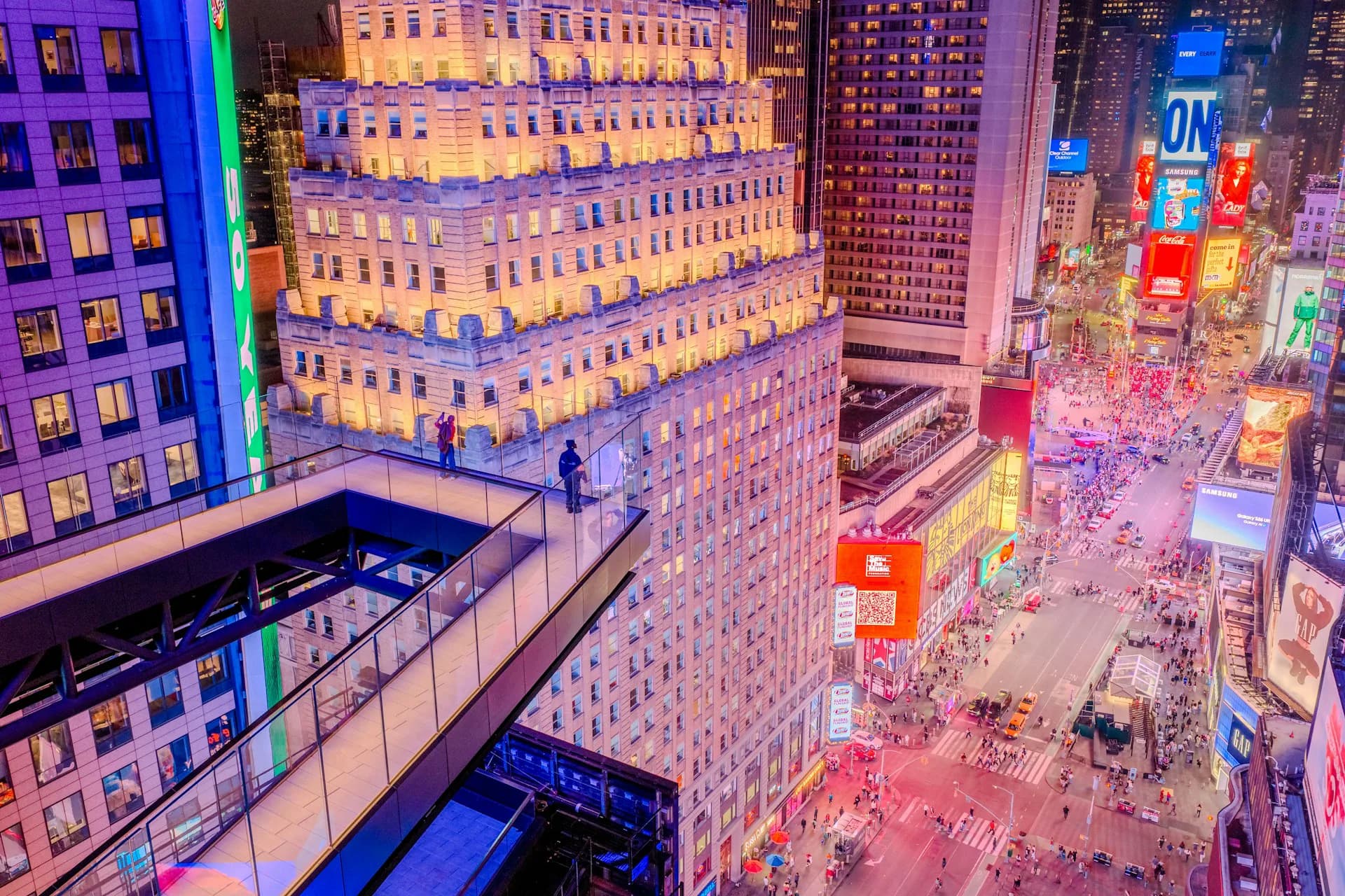 Aerial nighttime view of Times Square's illuminated buildings and bustling streets with vibrant signage and dense urban crowds by S9ARCHITECTURE.