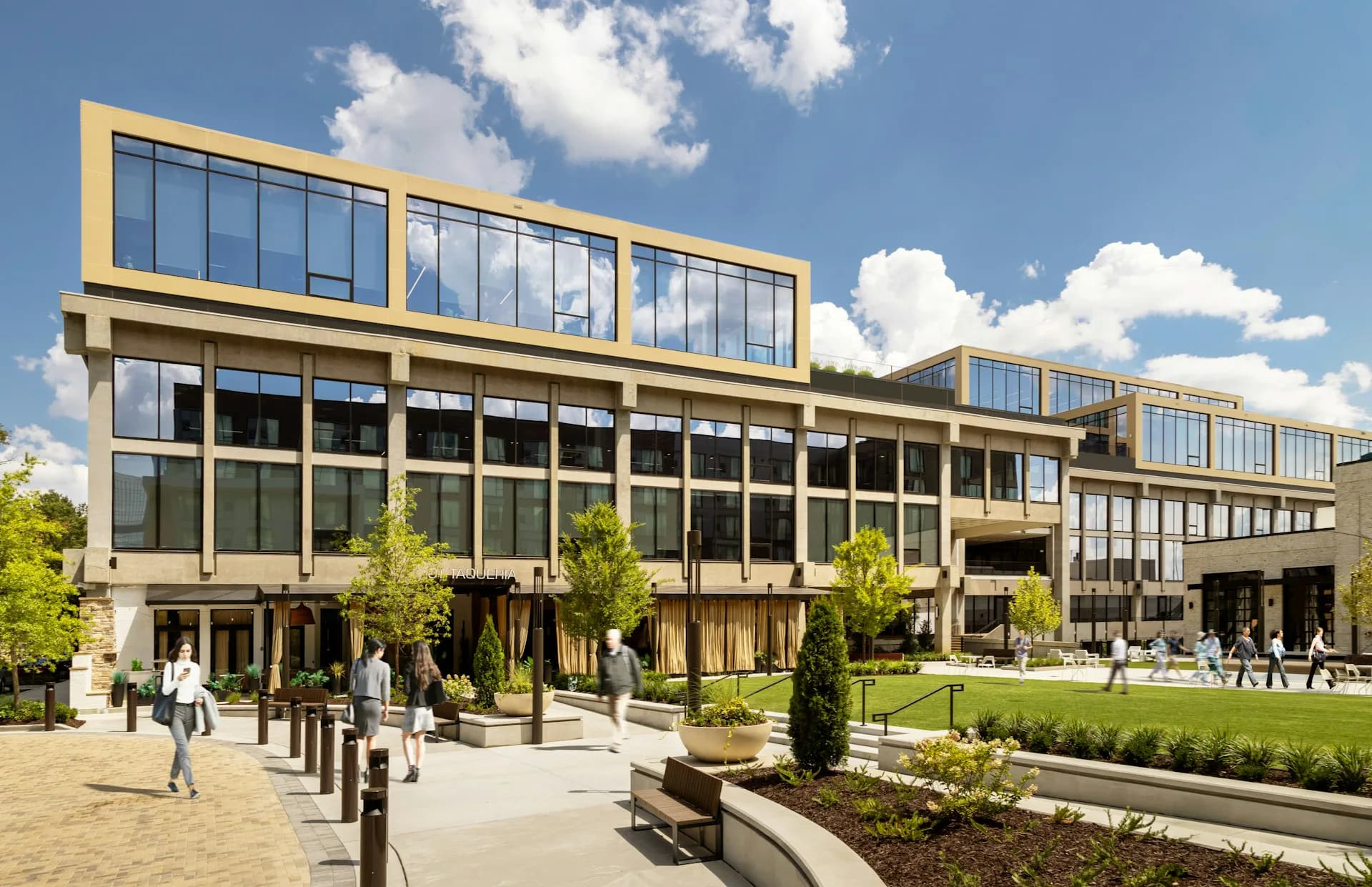 Contemporary multi-story institutional building with golden metal cladding, large glazed facades, and landscaped courtyard with seating areas by S9ARCHITECTURE.
