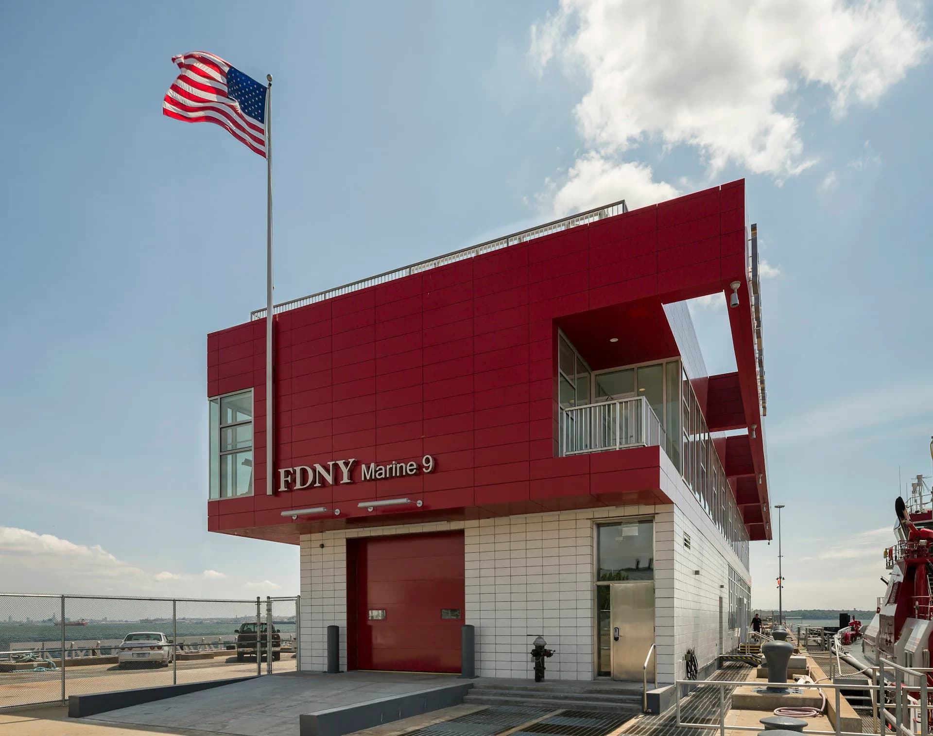 Red and white FDNY Marine 9 fireboat station with modern architecture featuring cantilever design and American flag, by Sage and Coombe Architects.