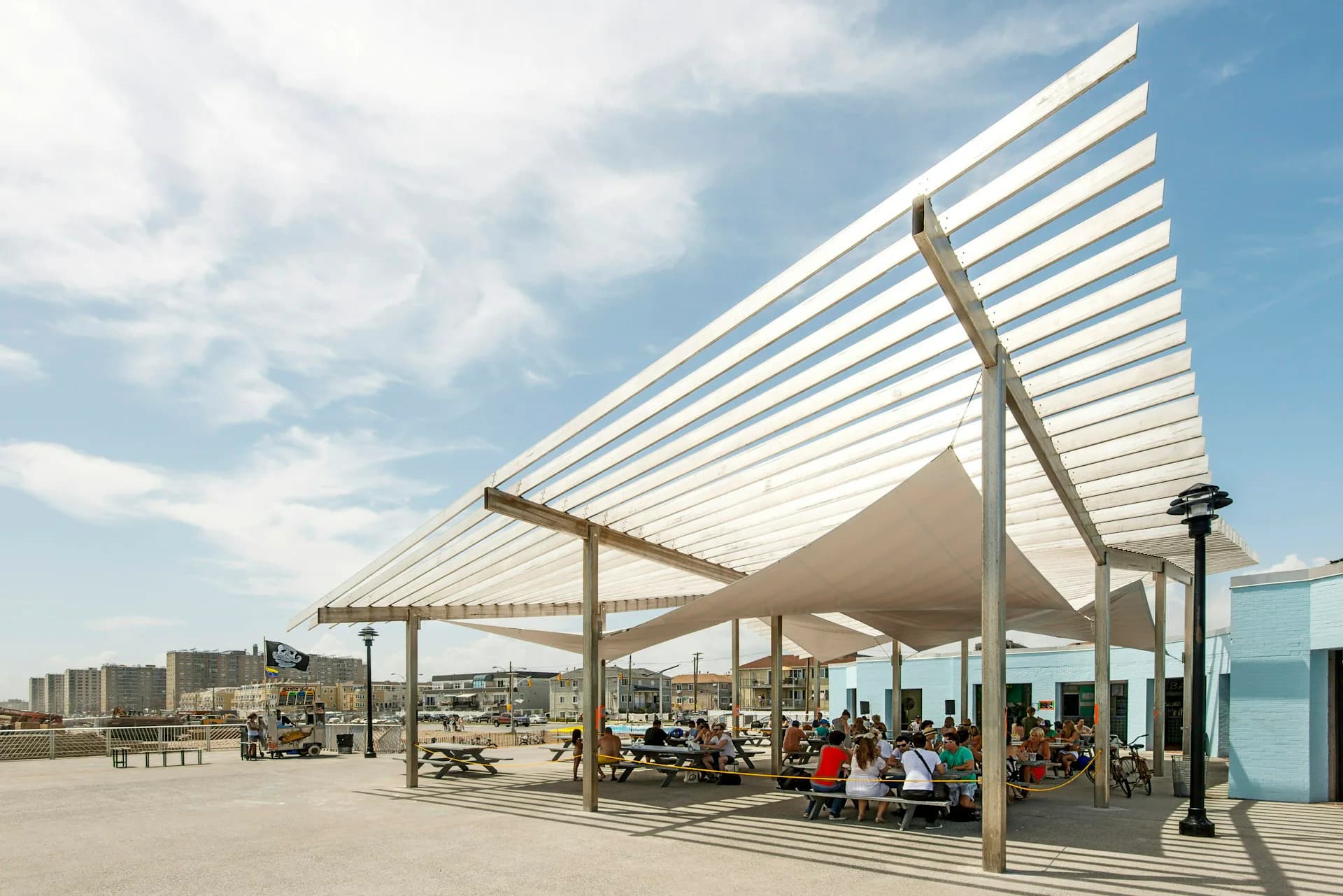 Modern waterfront pavilion with white striped canopy roof and steel columns sheltering outdoor seating area, designed by Sage and Coombe Architects.