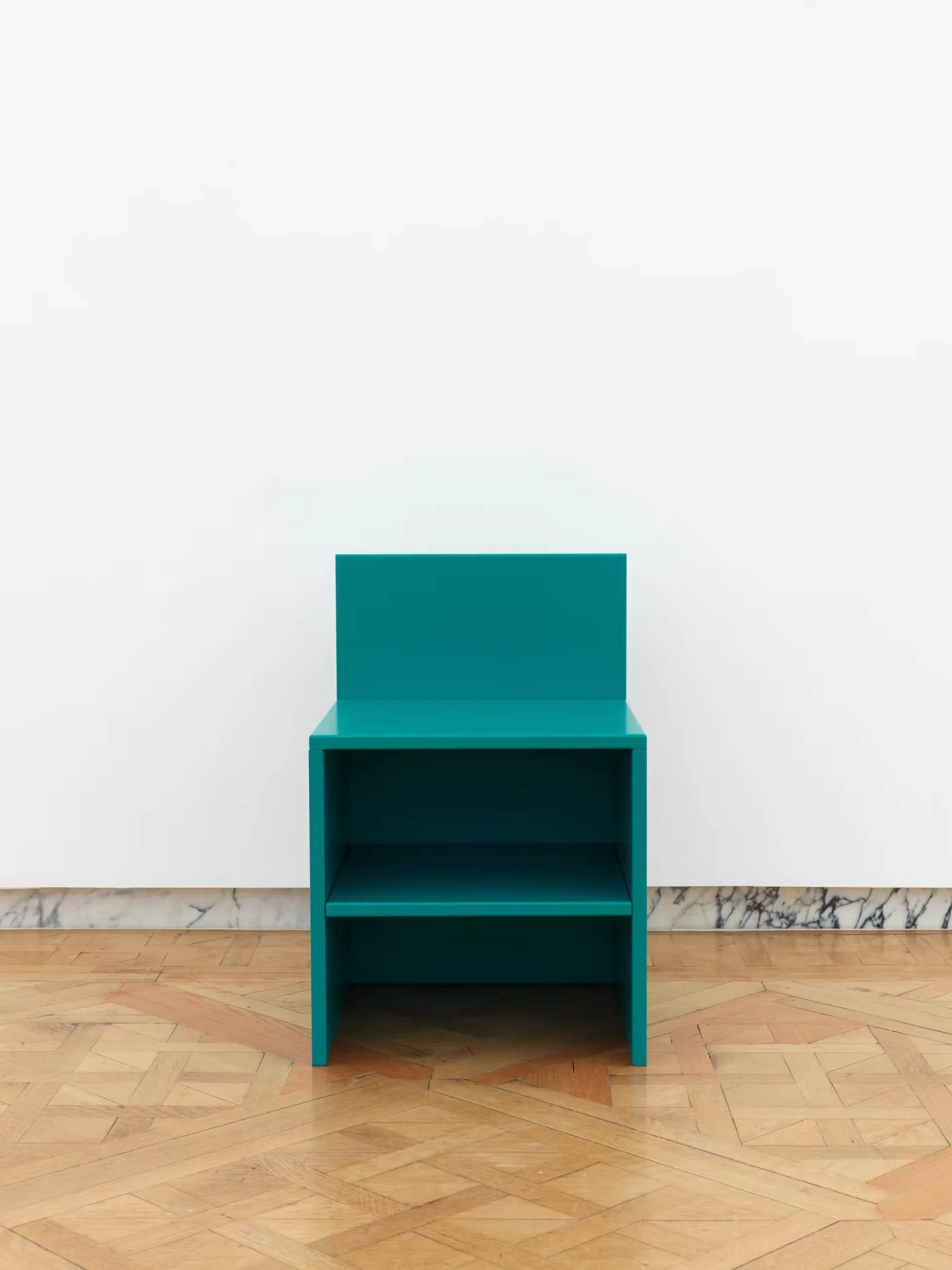 Teal-colored open shelving unit with geometric design on wooden parquet flooring against white wall by Salon 94 Design.