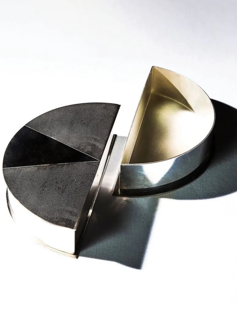 Sculptural metal bowls with curved geometric forms in polished steel and brass, casting dramatic shadows on white surface, by Sanayi313.