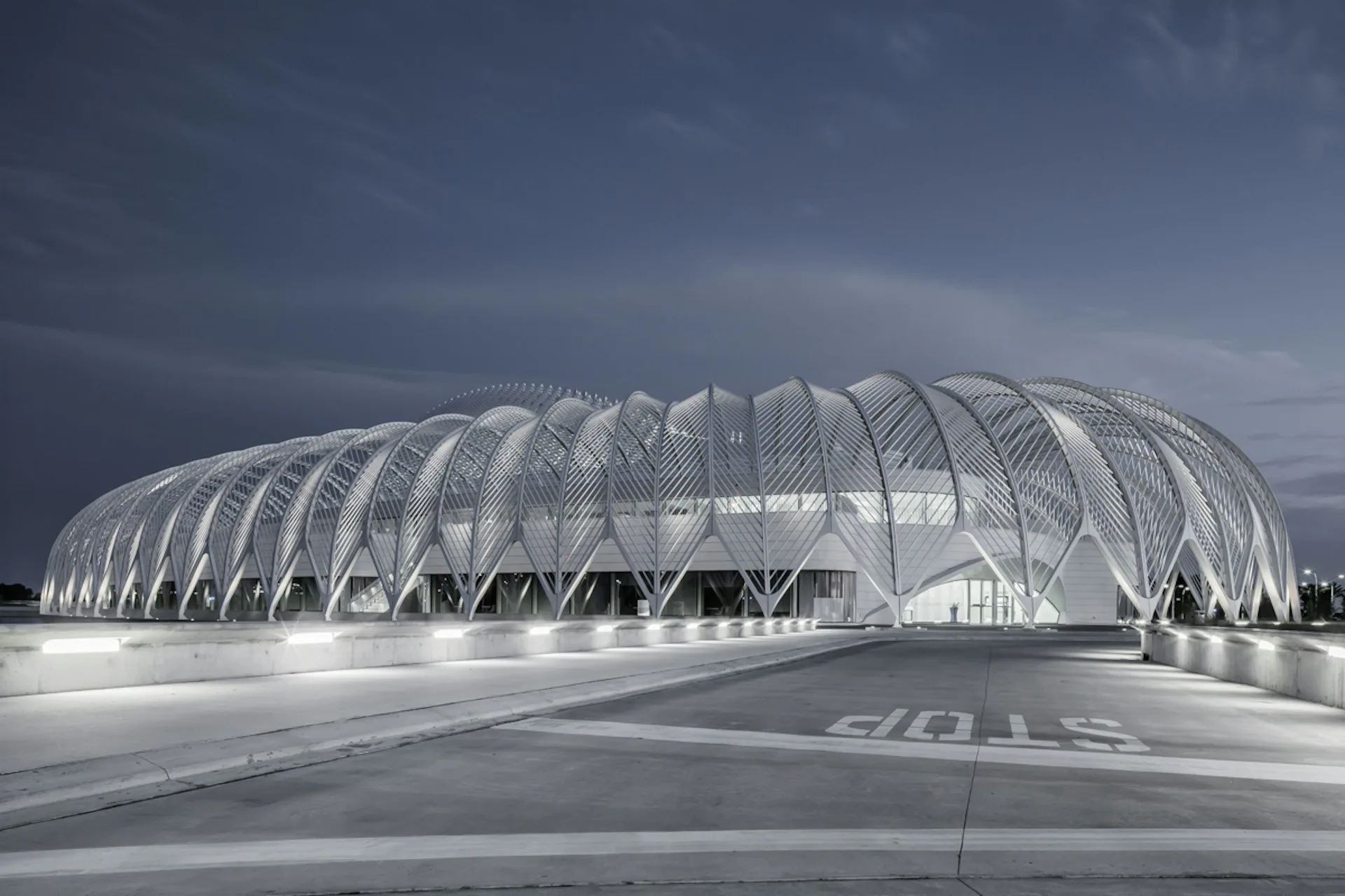 Ribbed structural shell building with white steel arches and mesh panels photographed under dramatic cloudy sky by SANTIAGO CALATRAVA.