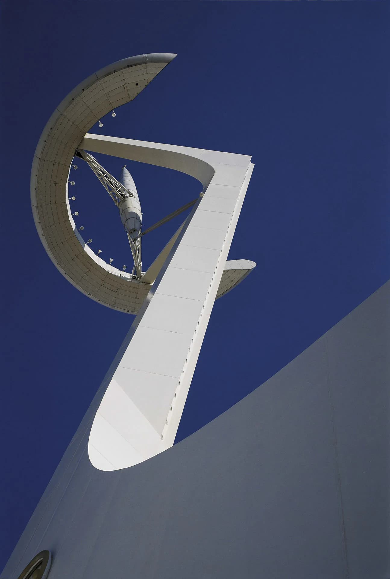 Architectural detail of a white sculptural tower element with an integrated clock mechanism featuring metallic curved framework against deep blue sky, by SANTIAGO CALATRAVA.