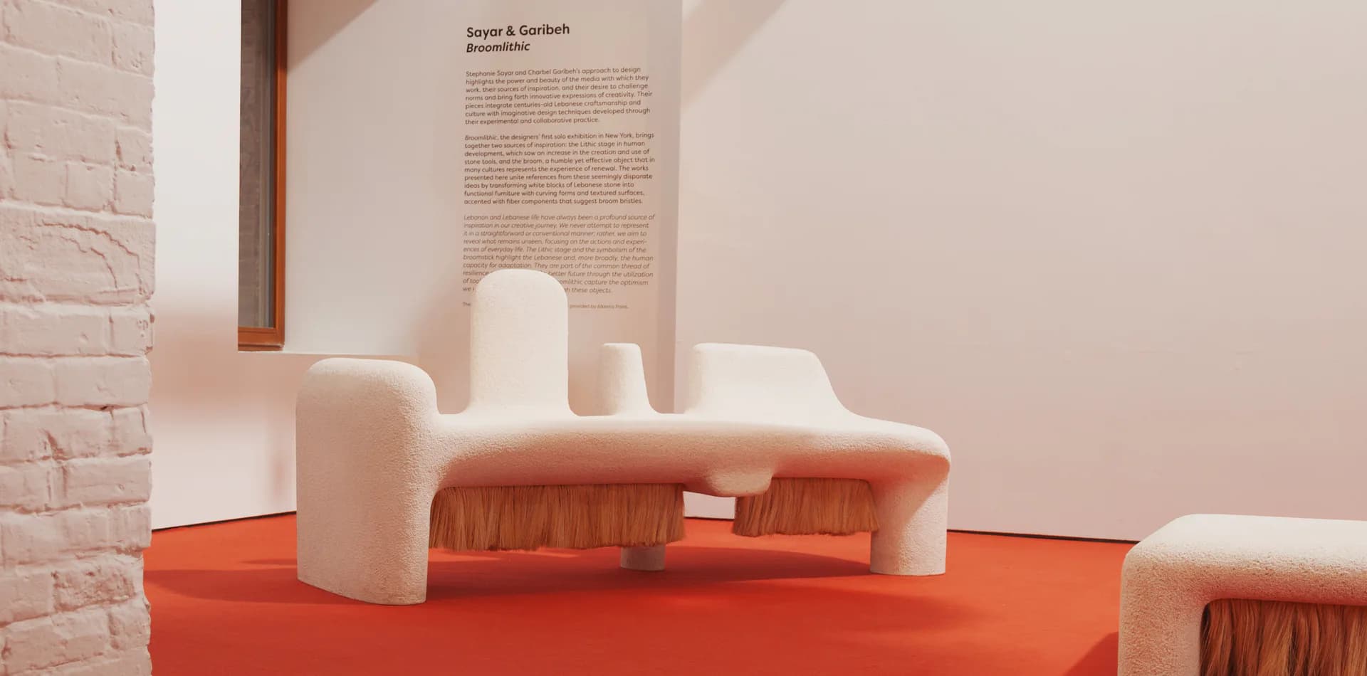Gallery installation with cream and terracotta forms on an orange platform, featuring a text panel on the beige wall, by Sayar & Garibeh.
