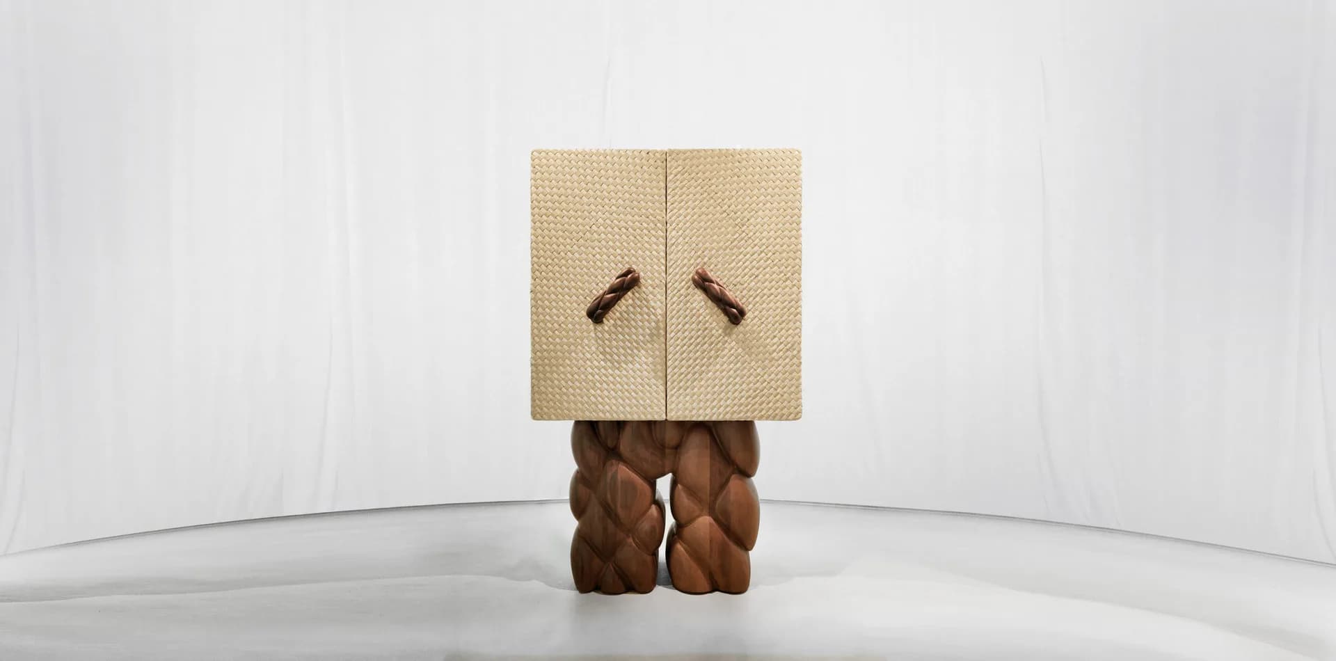 Sculptural figure with cardboard box head featuring drawn eyes and brown wooden body, installed in minimalist white gallery space by Sayar & Garibeh.