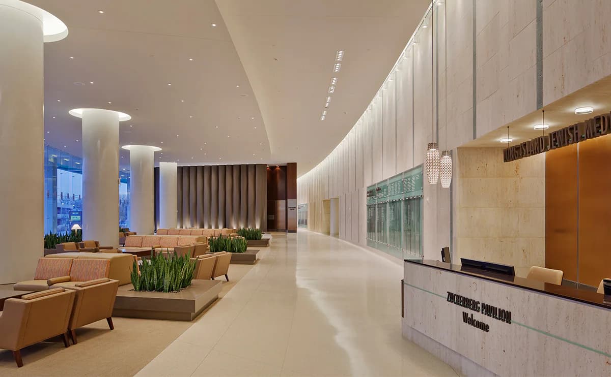 Modern hotel lobby with polished concrete floors, illuminated vertical wall panels, cylindrical columns, and a reception desk, designed by SBLD Studio.