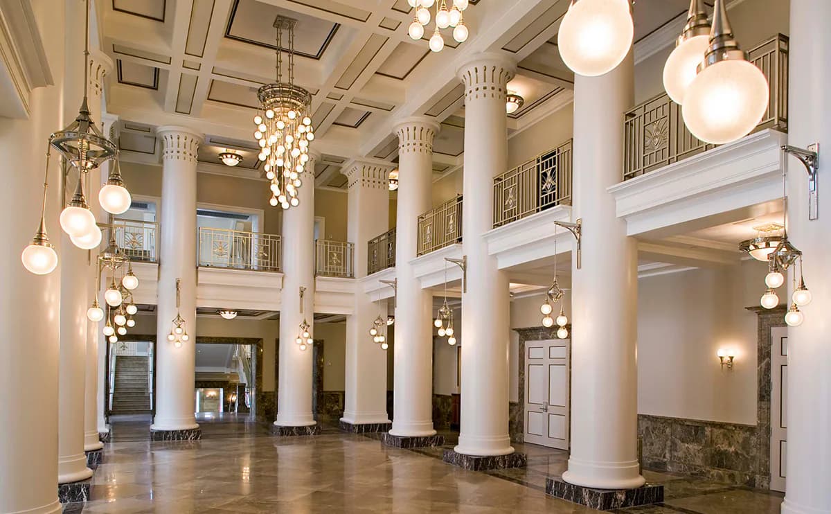 Grand neoclassical lobby with soaring columns, coffered ceiling, pendant globe lights, and polished floors by SBLD Studio.