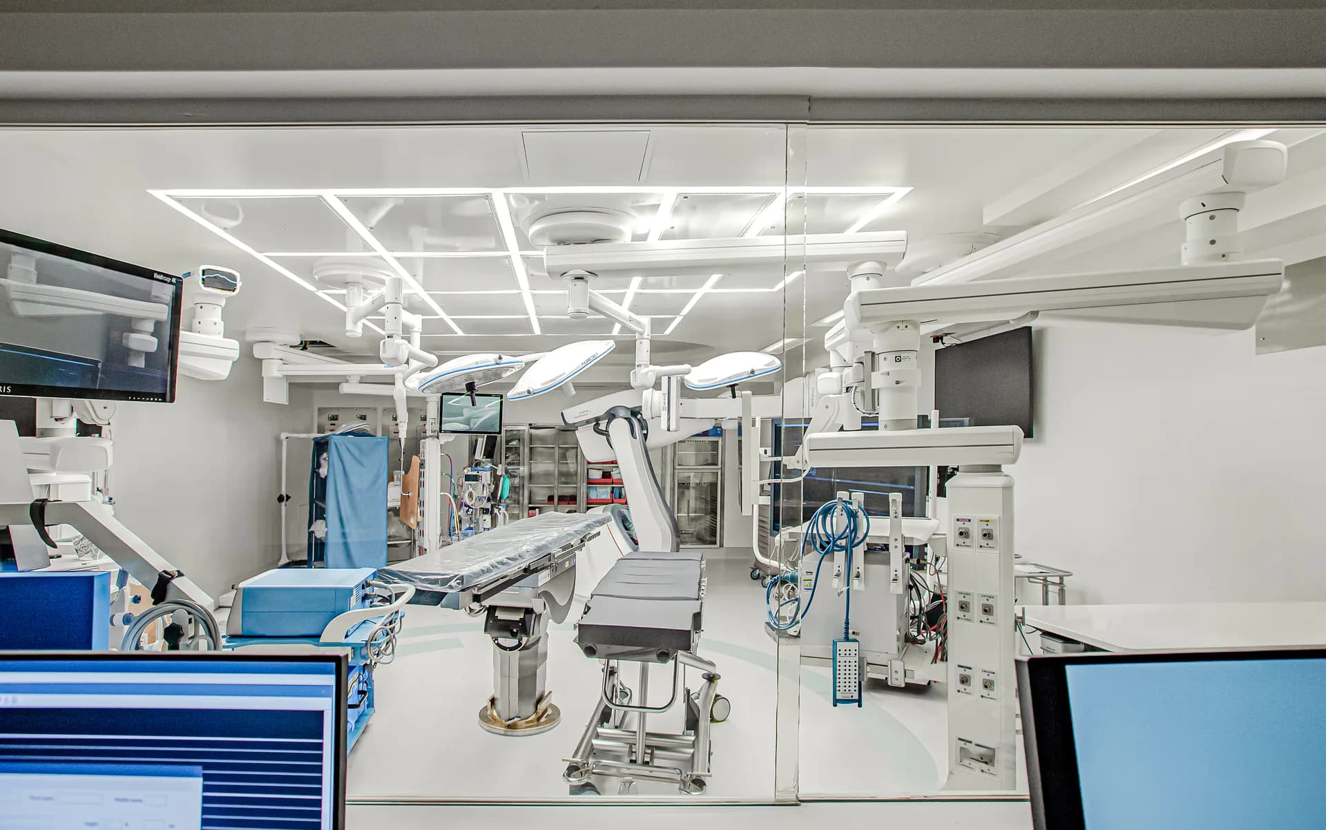 Modern surgical operating room with bright LED ceiling lights, sterile white walls, advanced medical equipment, and blue cabinetry by SBLM Architects.