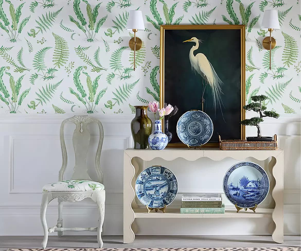 Elegantly styled vignette featuring fern-patterned wallpaper, white shelving with blue and white ceramics, botanical artwork, and period furniture by Scalamandré.