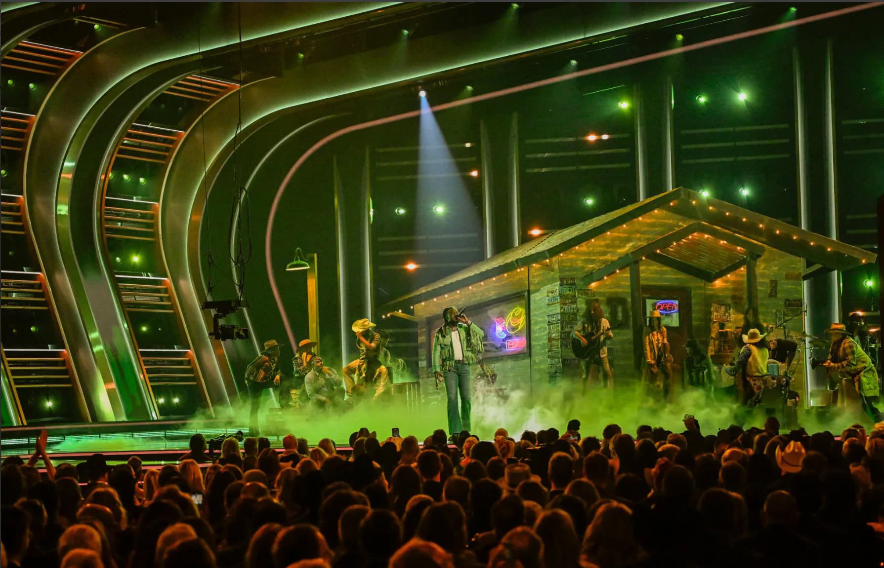 Green-lit theatrical stage set with nativity scene structure and dramatic lighting design surrounded by audience, by Scenicorp.