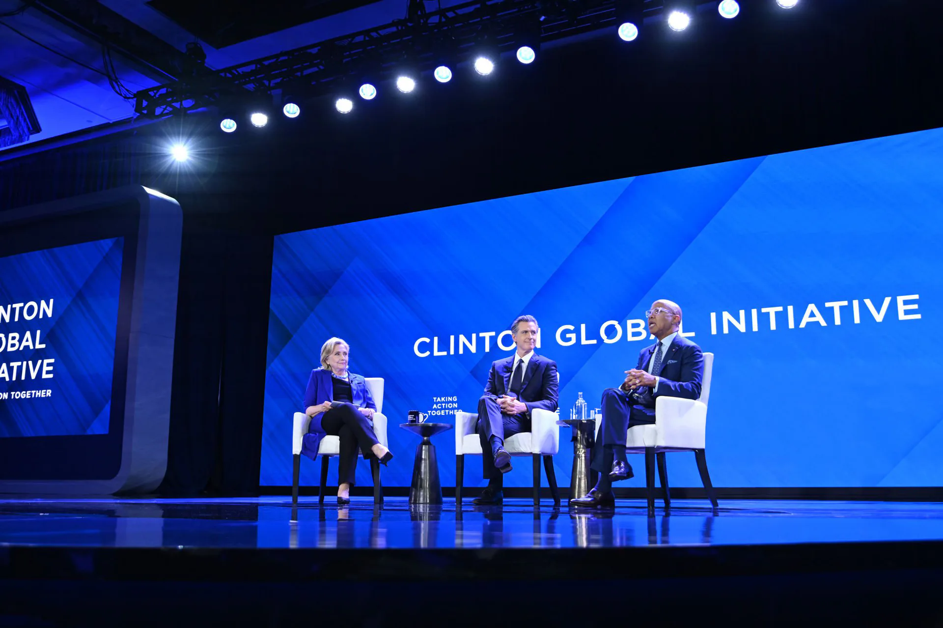Blue-lit conference stage with panel seating, professional lighting rig, and Clinton Global Initiative branding by Scenicorp.