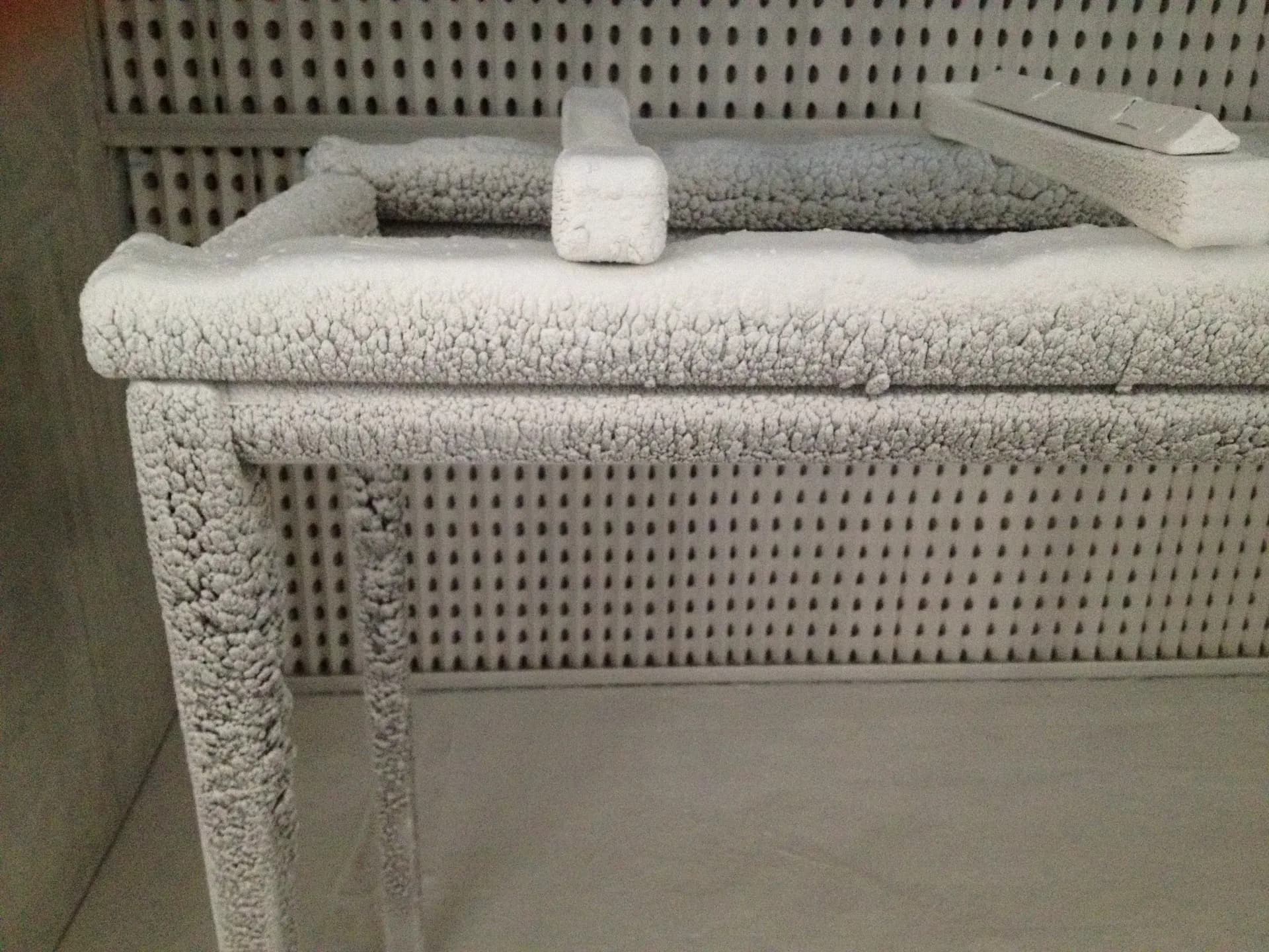 Minimalist interior with textured gray upholstered furniture, white towel rolls, and perforated wall paneling creating a serene, monochromatic spa-like environment by Schematic.