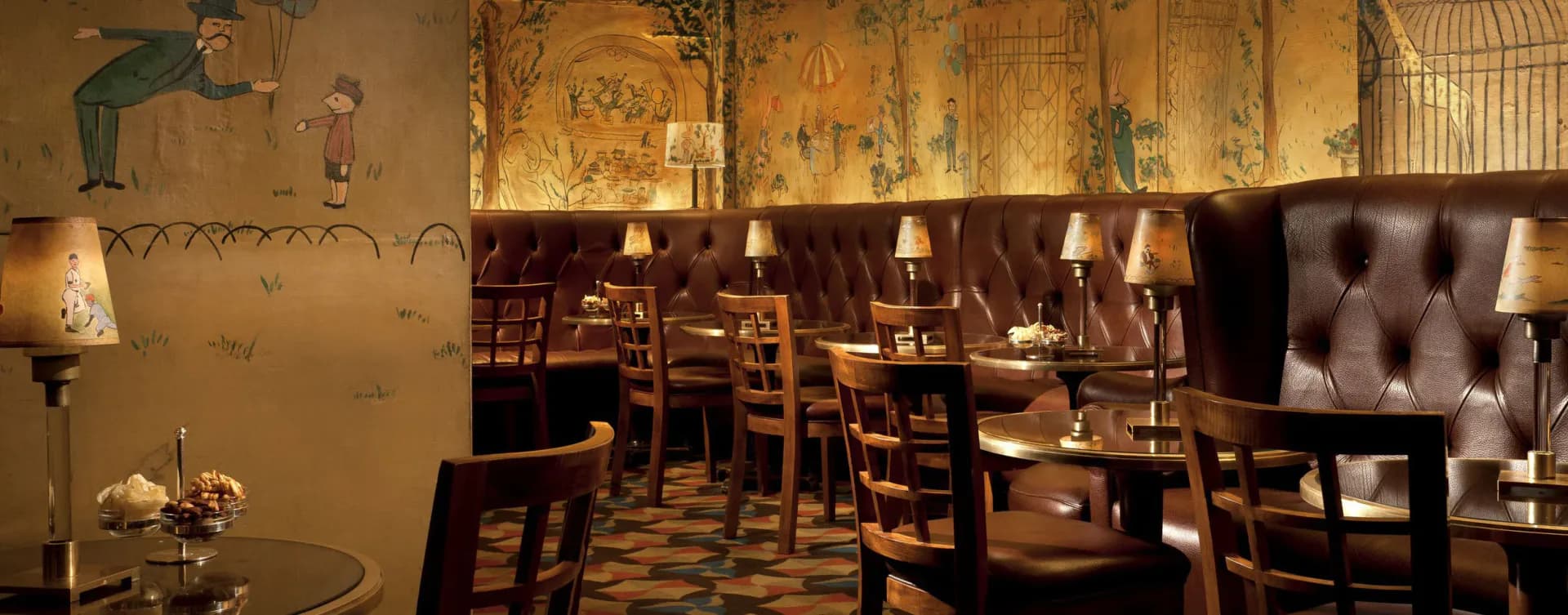 Warm-toned bar interior with tufted burgundy seating, wooden chairs, exposed brick, and layered ambient lighting by Schwinghammer Lighting.