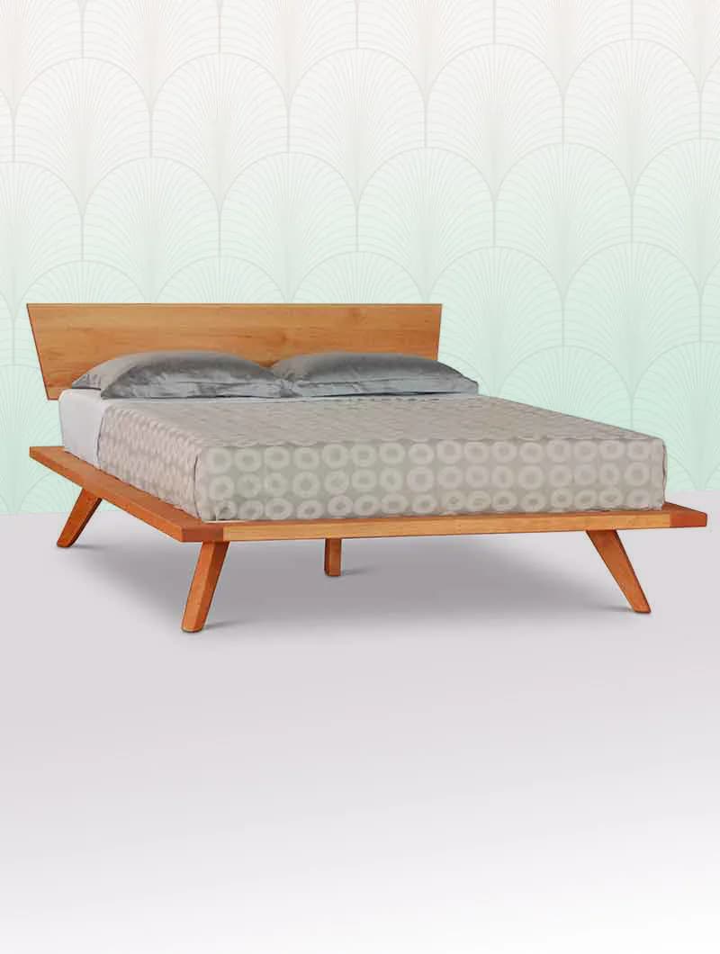 Mid-century modern wooden bed with angled legs and upholstered headboard, displayed against a patterned wallpapered backdrop by Scott Jordan Furniture.